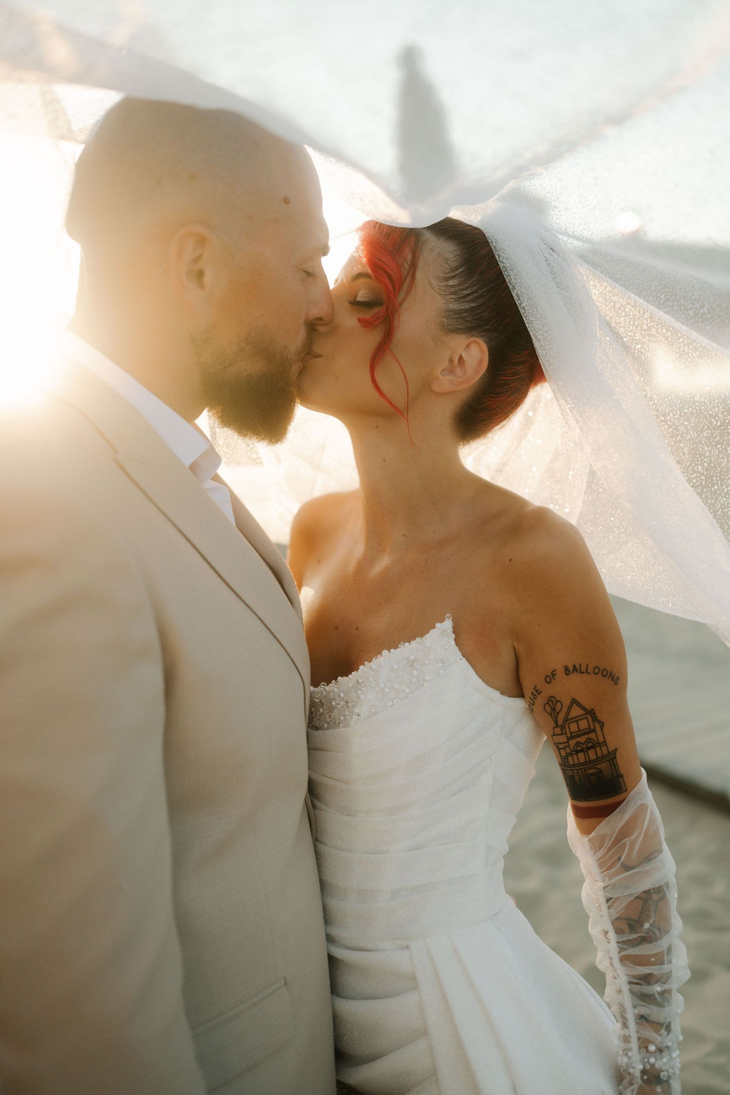 A couple in wedding attire share an intimate moment in soft sunlit lighting.