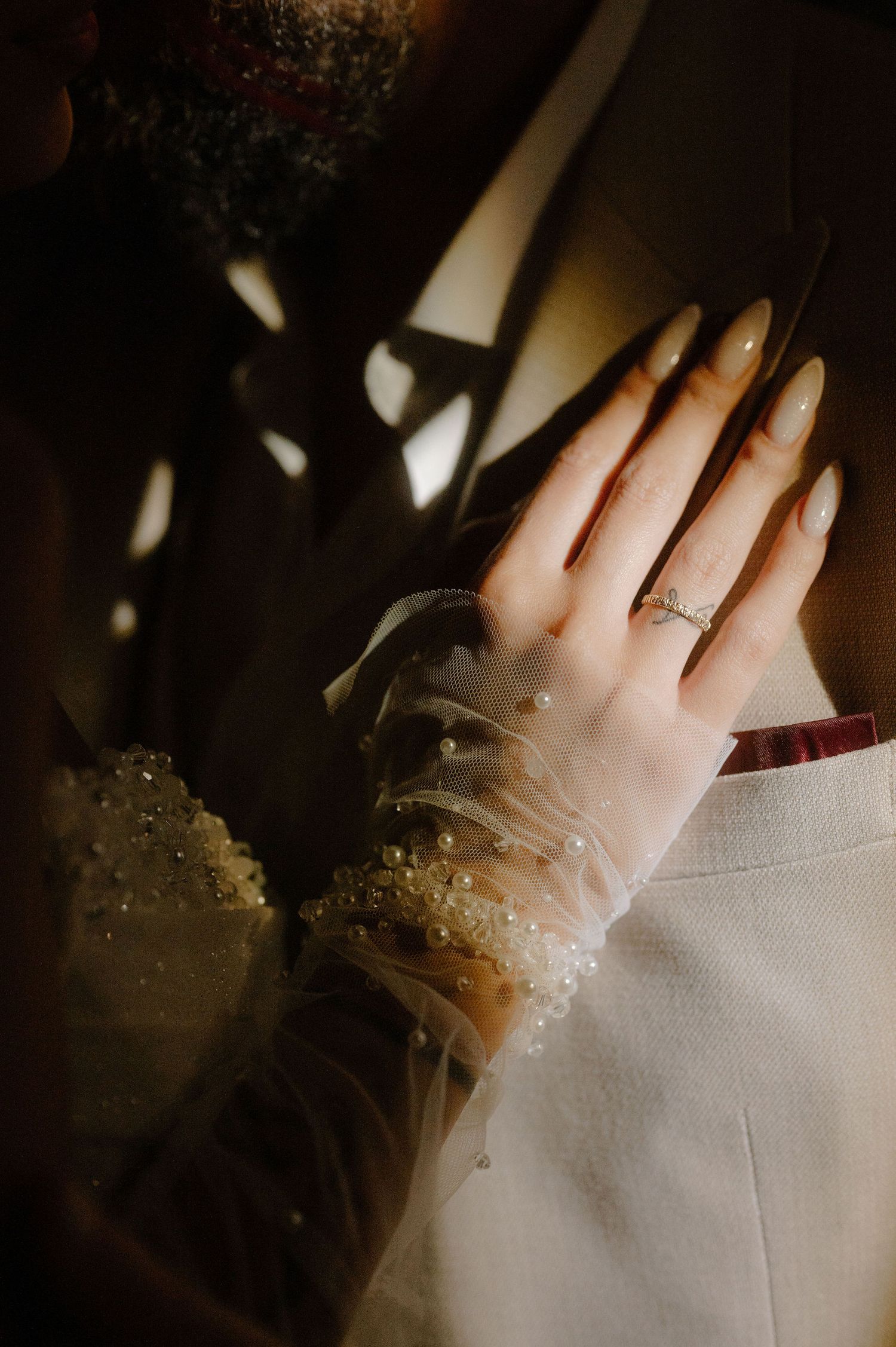 A hand wearing a delicate engagement ring sparkles in dramatic lighting against a dark background.