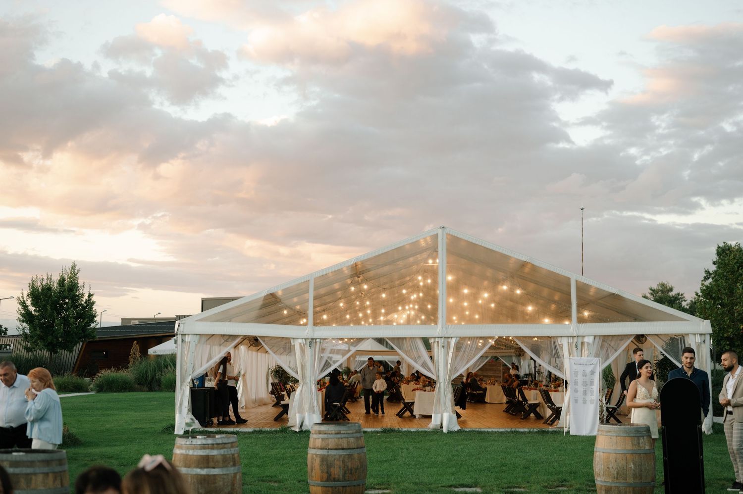 White wedding tent illuminated at sunset with string lights creating a romantic outdoor reception atmosphere.