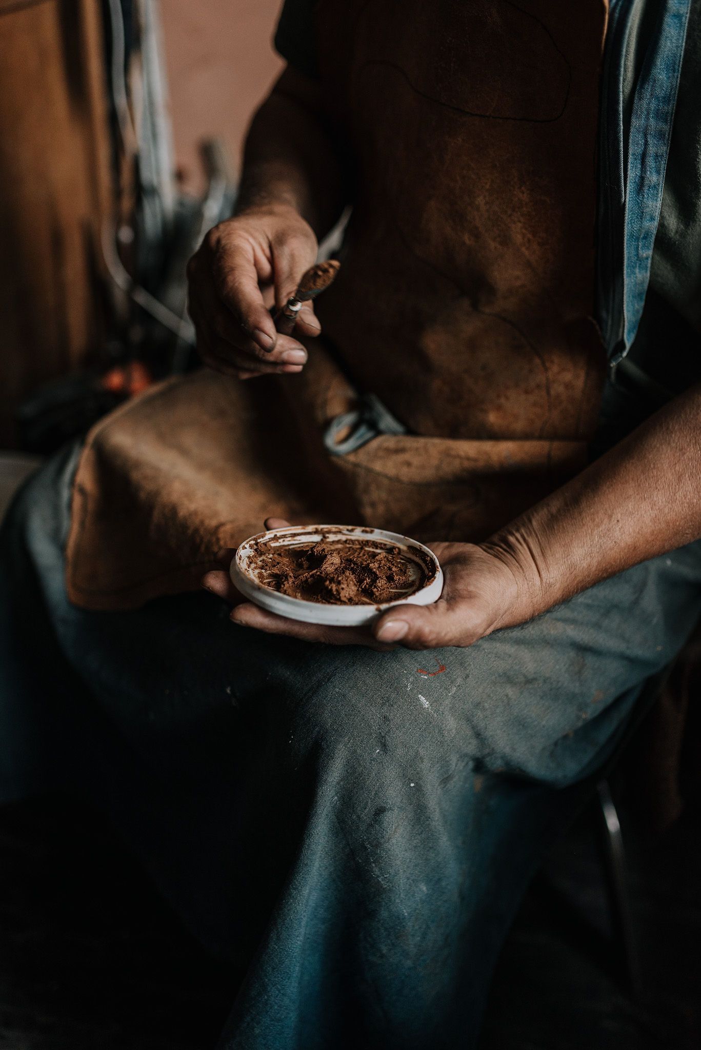 Hands hold a plate with dark material in moody lighting.