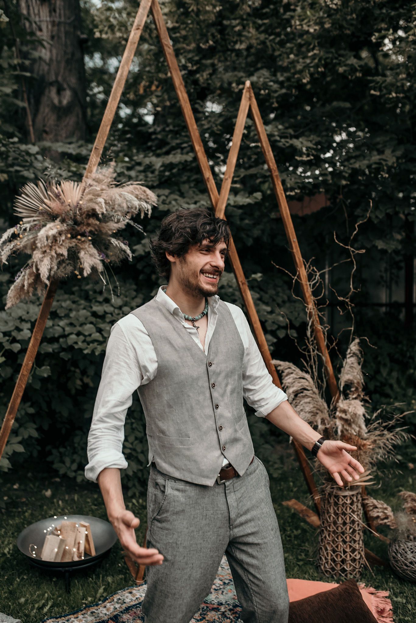 A person in vintage-style clothing laughs joyfully while standing near wooden frames in a garden setting.