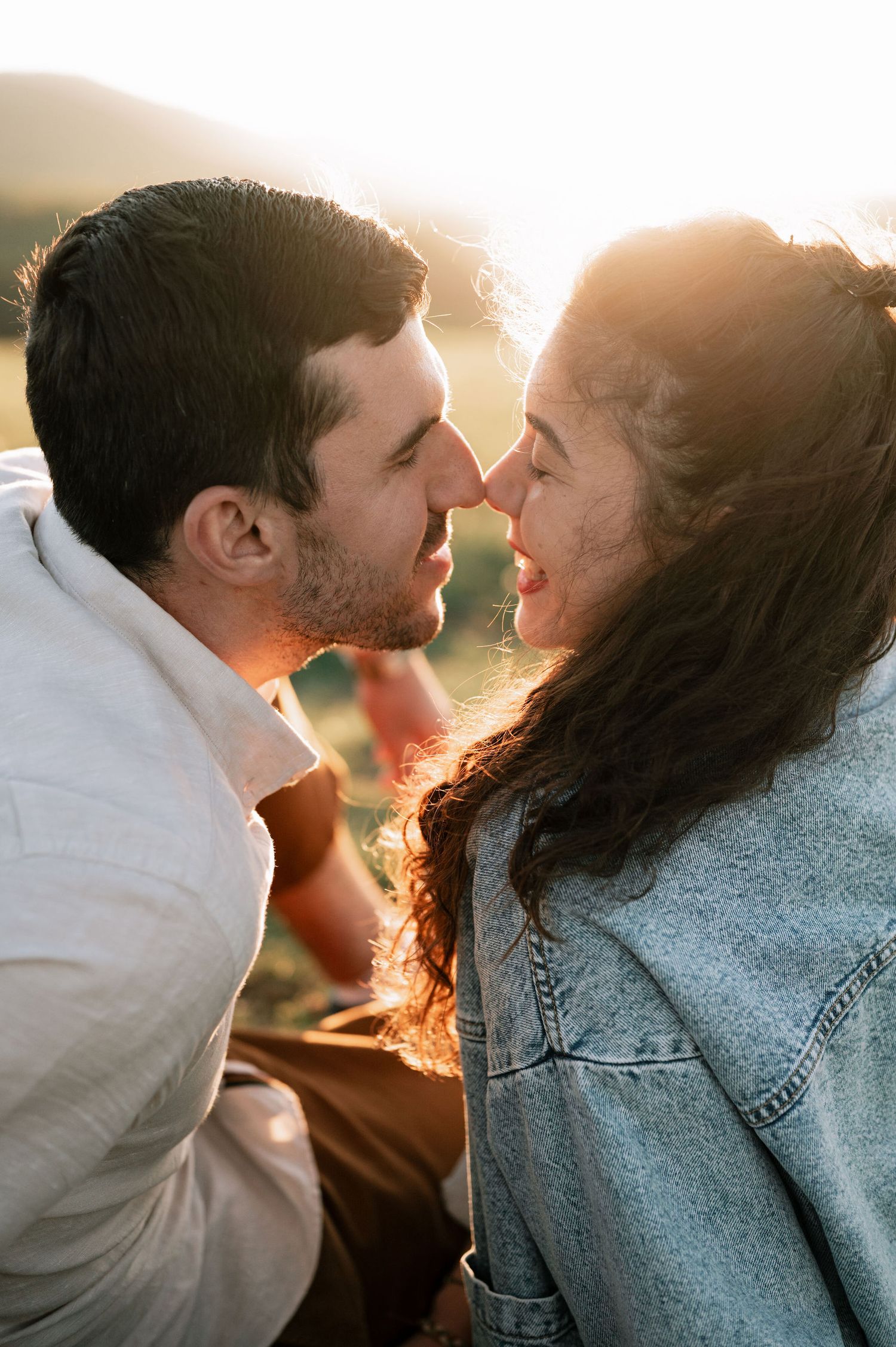 A romantic couple shares tender moments at sunset with sunlight creating a warm backlit glow through their silhouettes.