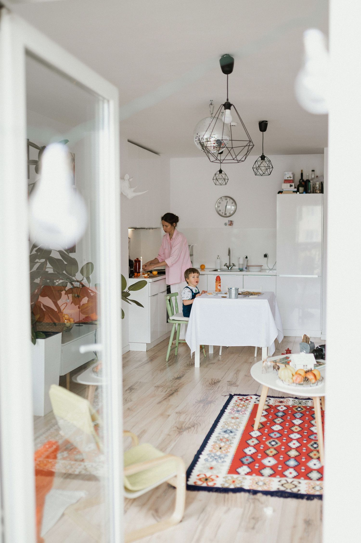 Modern minimalist white dining room with geometric pendant lights and light wood flooring.