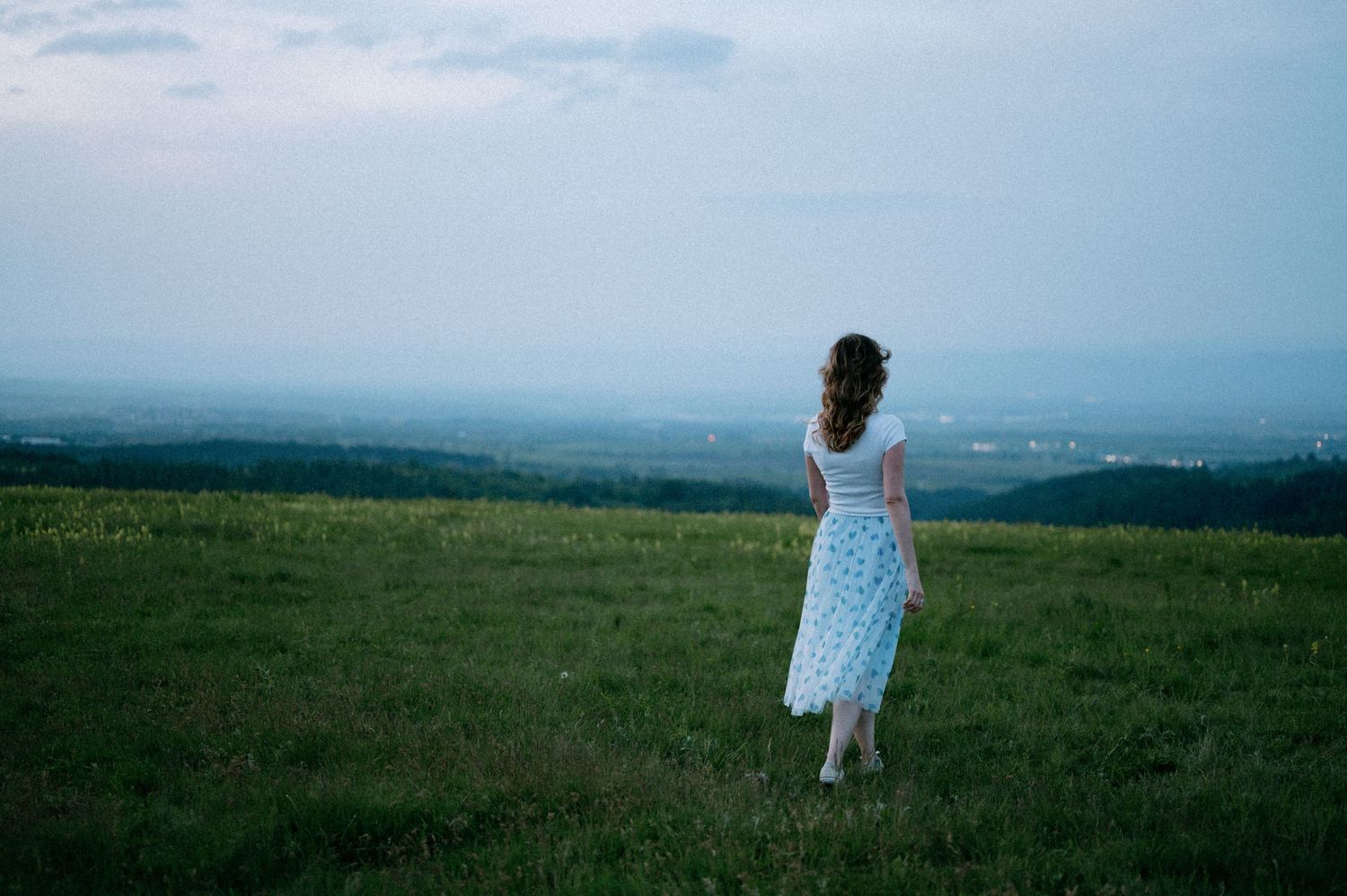 A person in a flowing dress stands on a hilltop overlooking a misty valley.