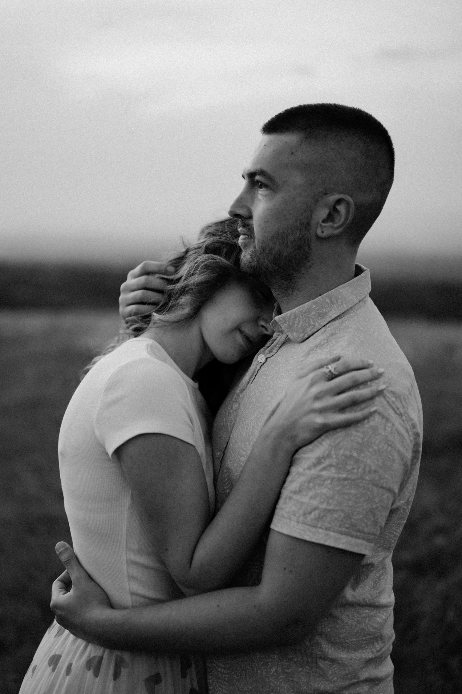 An intimate black and white photo of a couple embracing in a field.