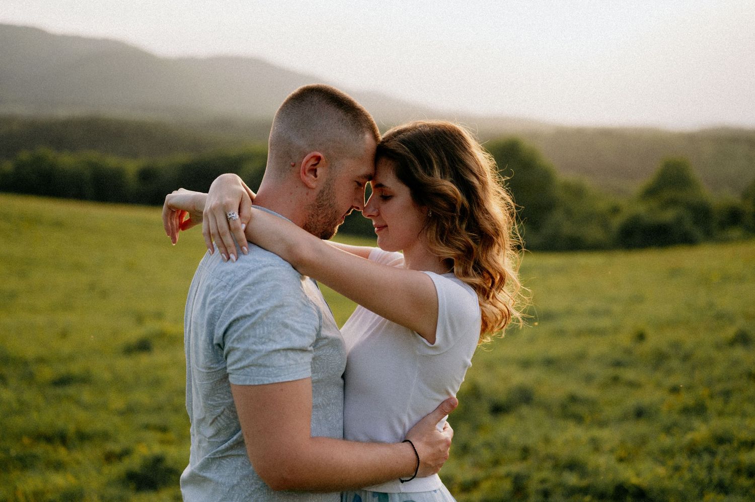 Intimate couple dancing together in a green field at sunset.