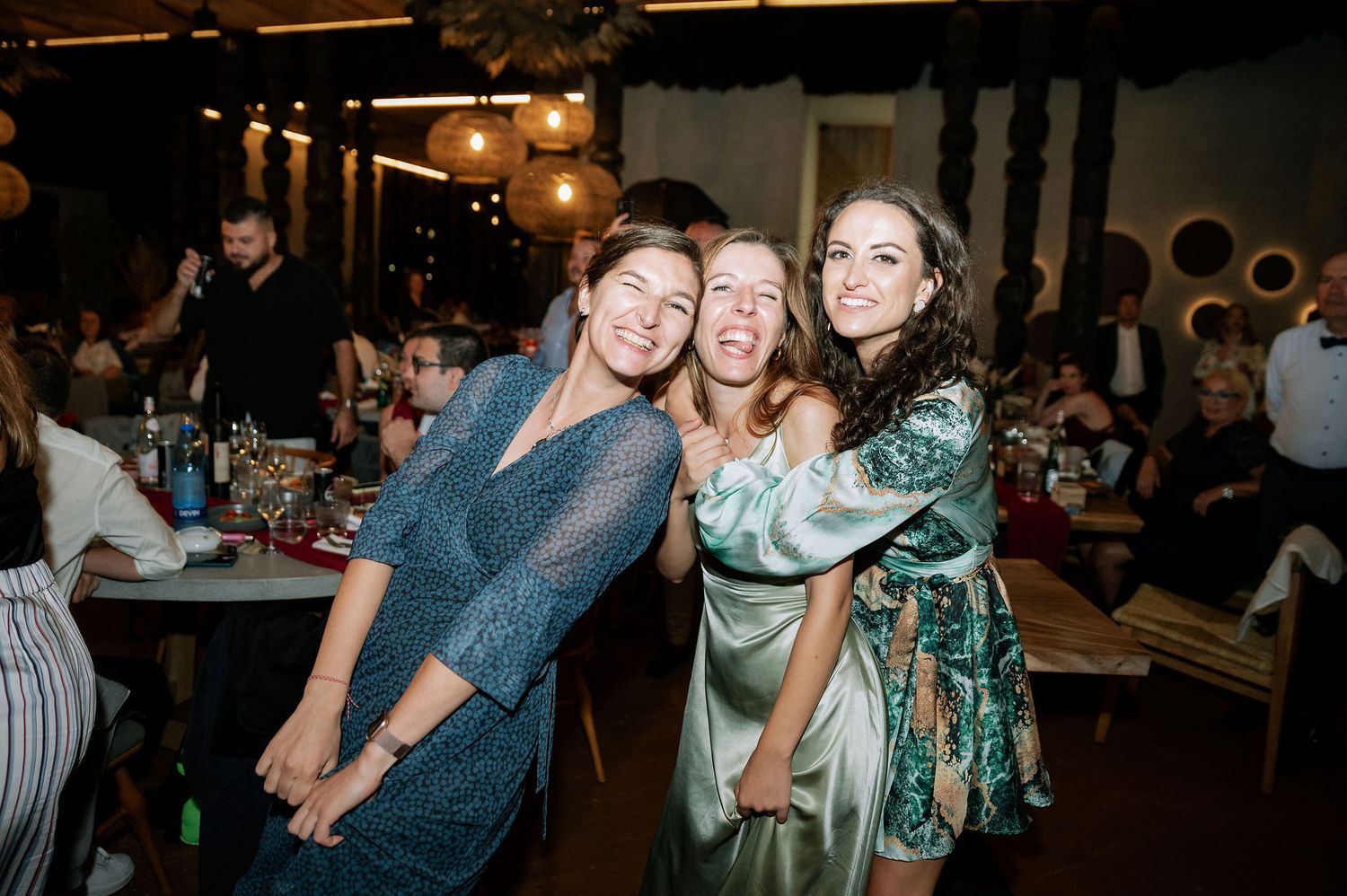 Wedding guests dancing and celebrating on a dimly lit dance floor with paper lanterns overhead.