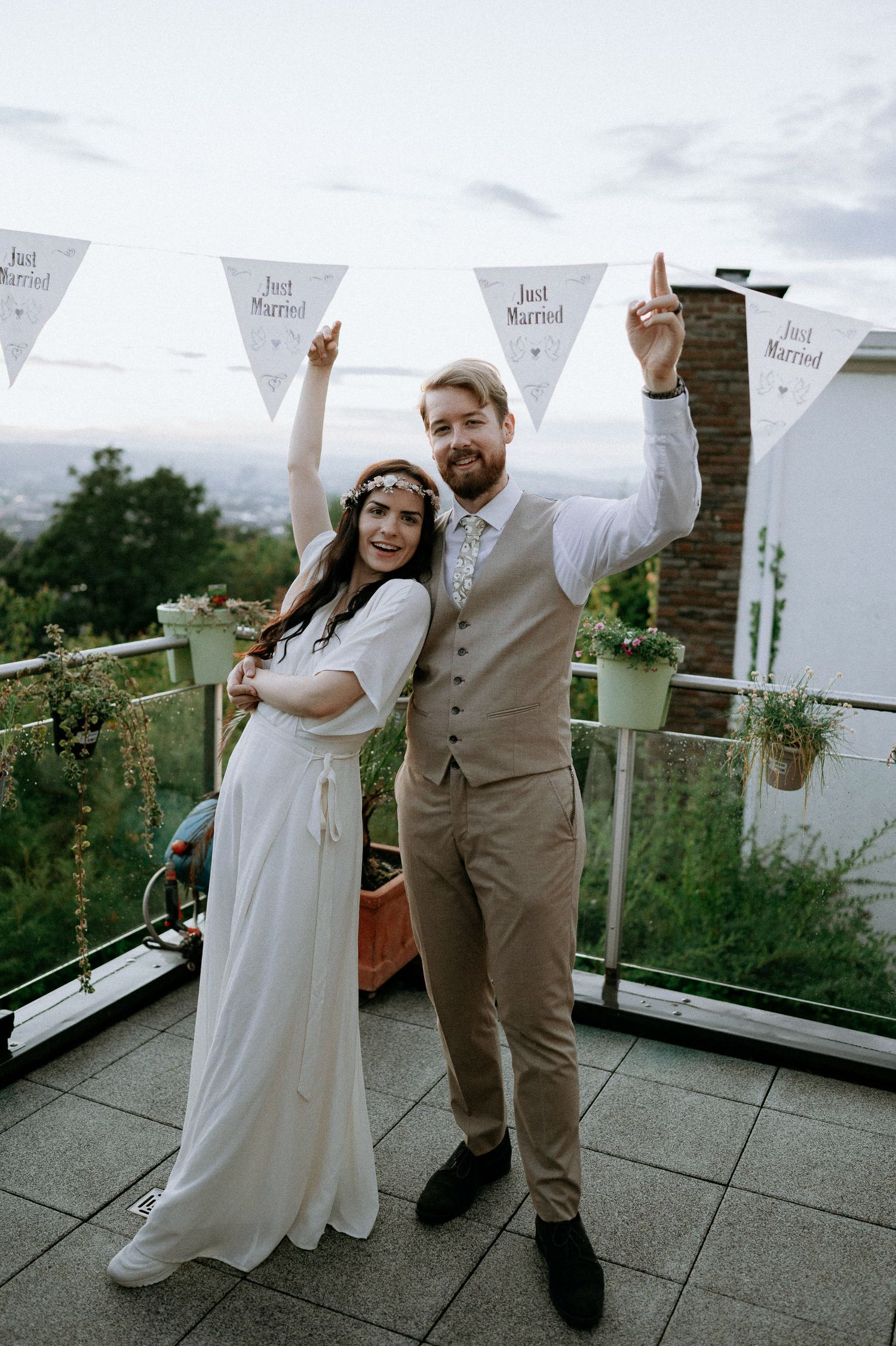 A couple in wedding attire poses playfully with white banners on an outdoor terrace.