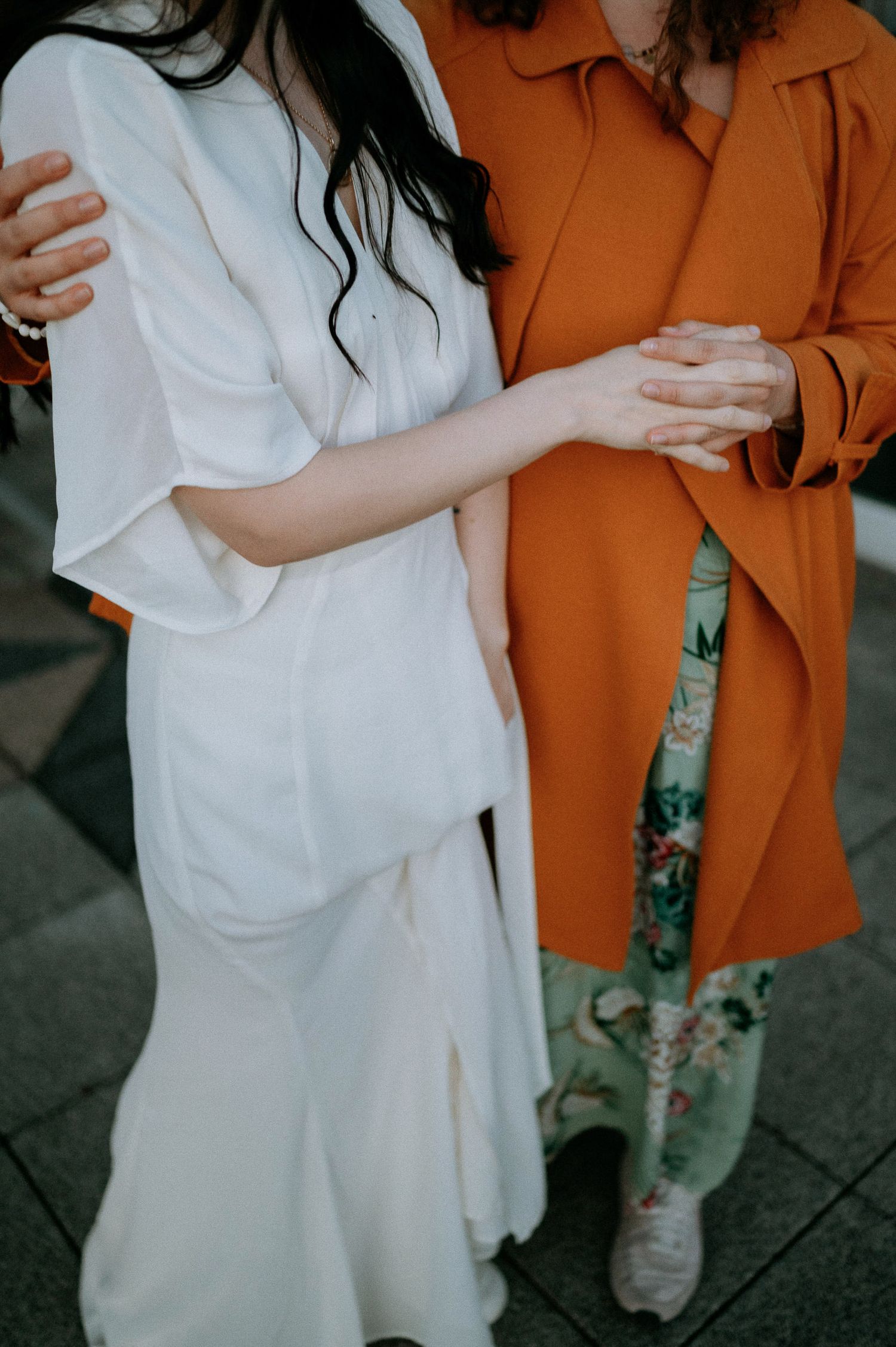 Friends in white and burnt orange outfits embracing and laughing together.
