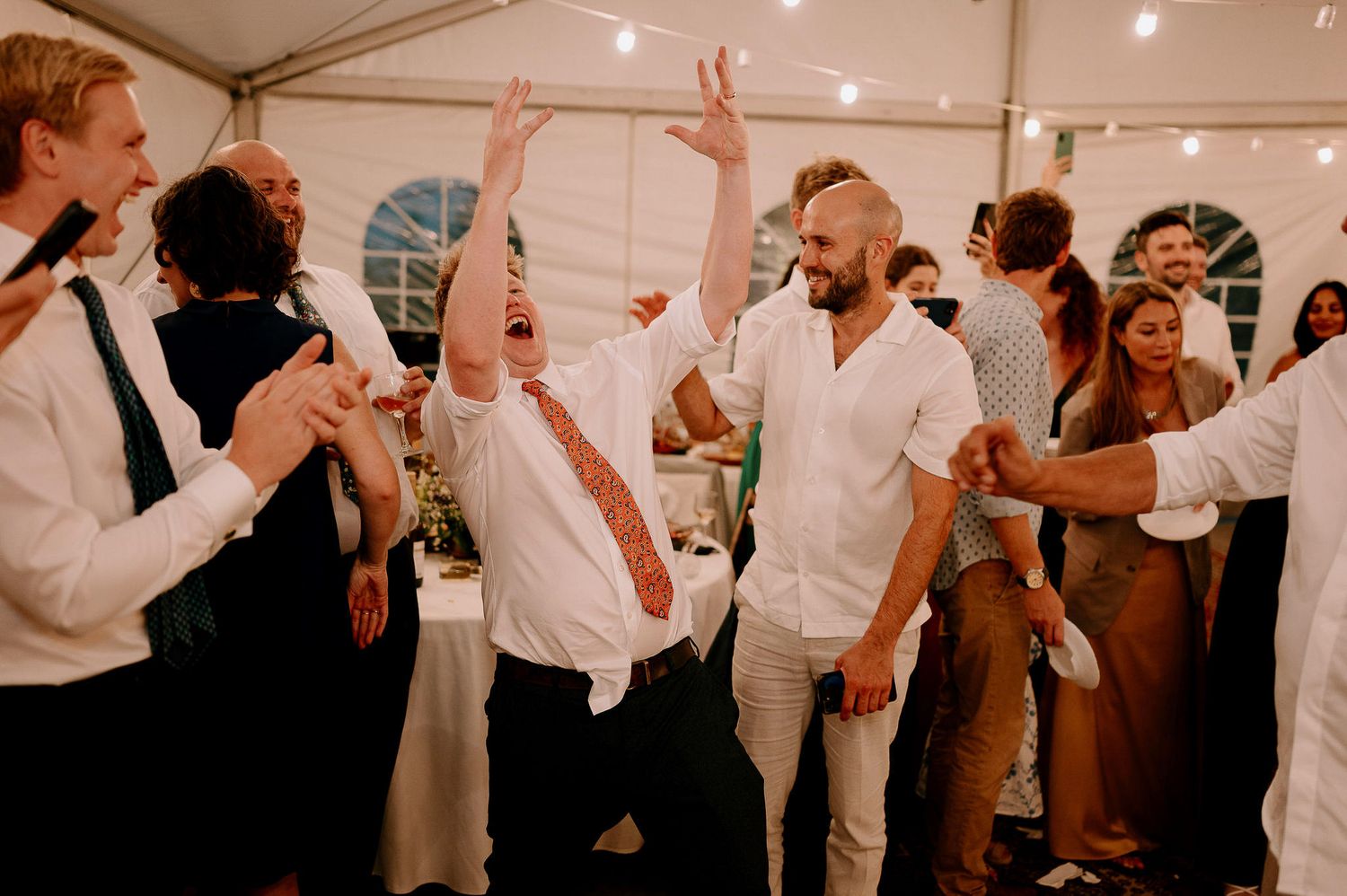 Energetic party scene with guests dancing and celebrating under tent lighting.