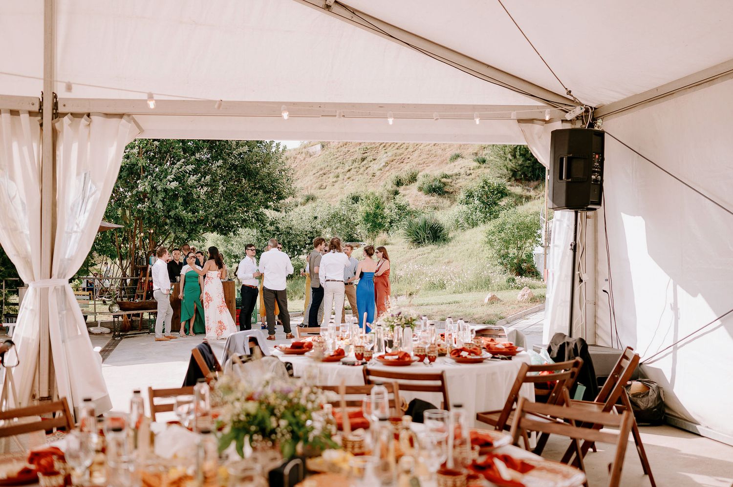 A wedding reception tent setup with decorated tables and scenic mountain views in the background.