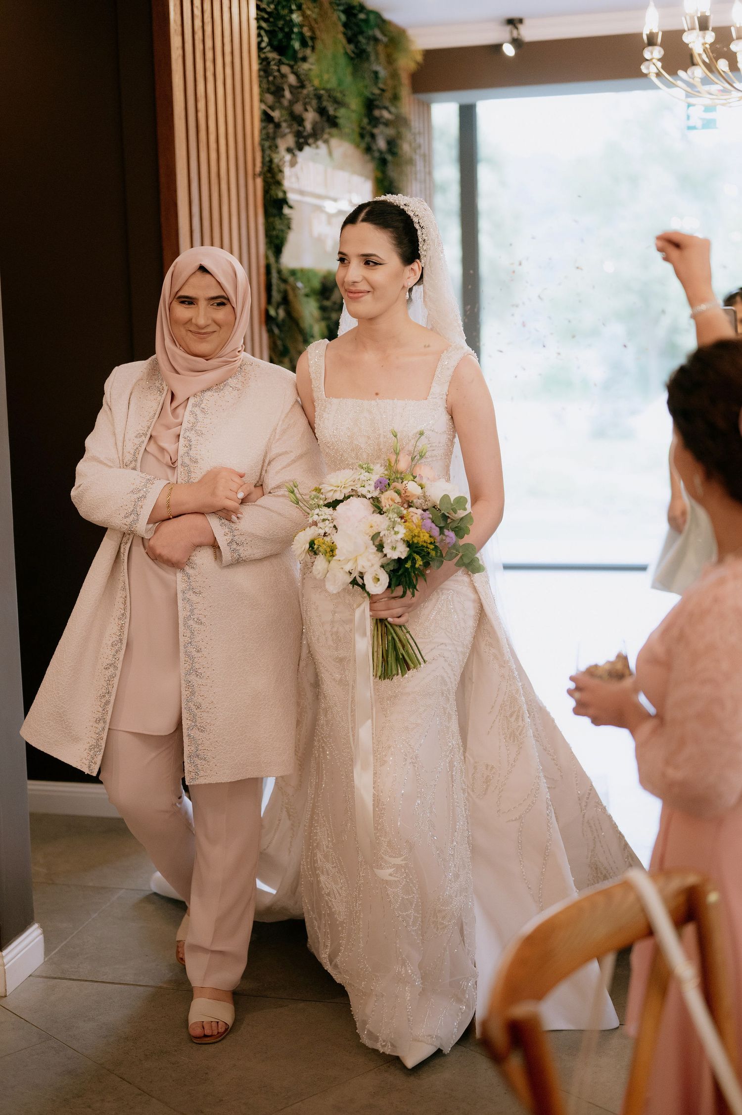 Wedding party members in light-colored formal attire pose in an elegant venue with chandeliers.