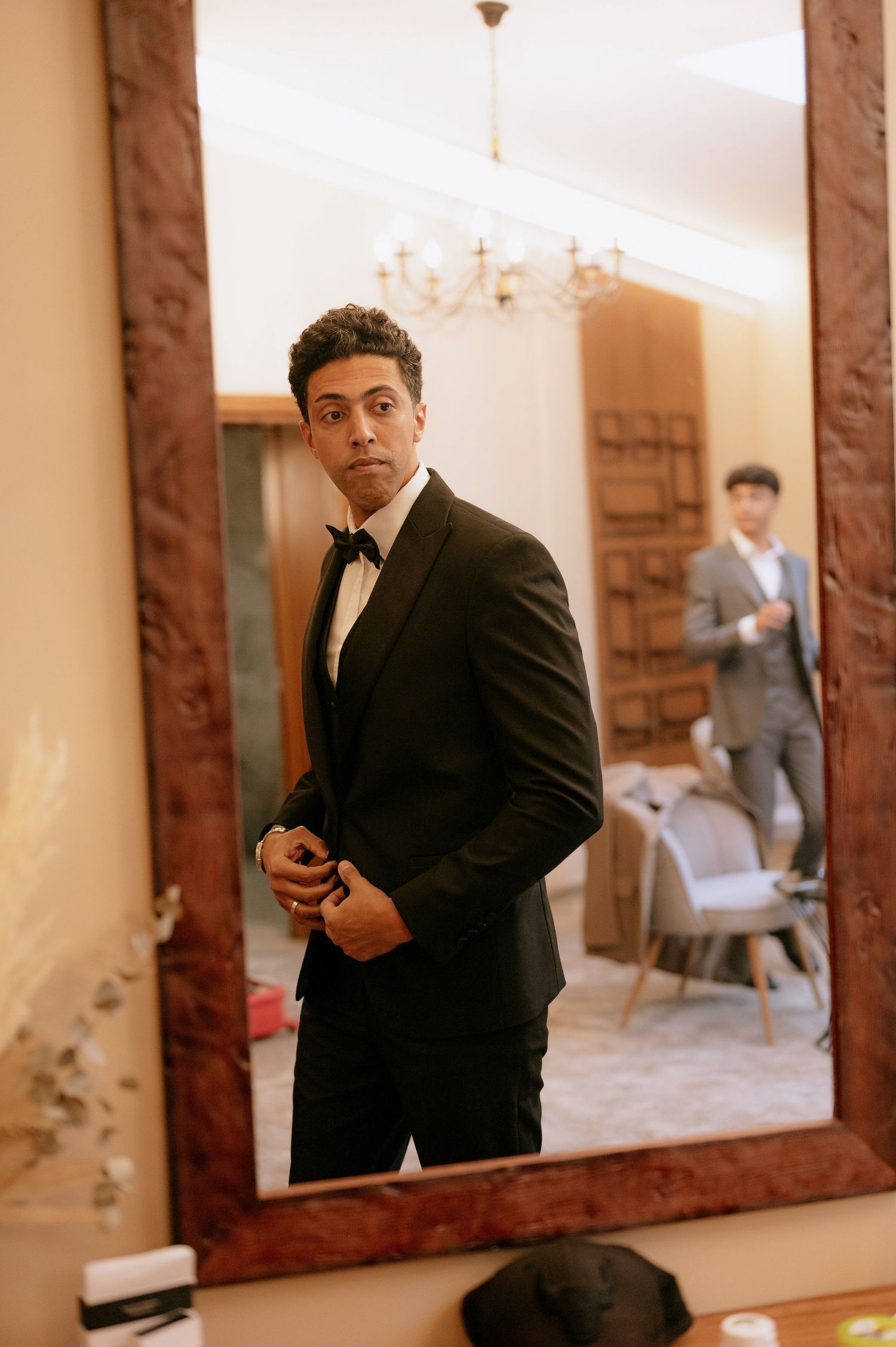 Elegant mirror reflection showing someone adjusting formal attire in a well-lit room.