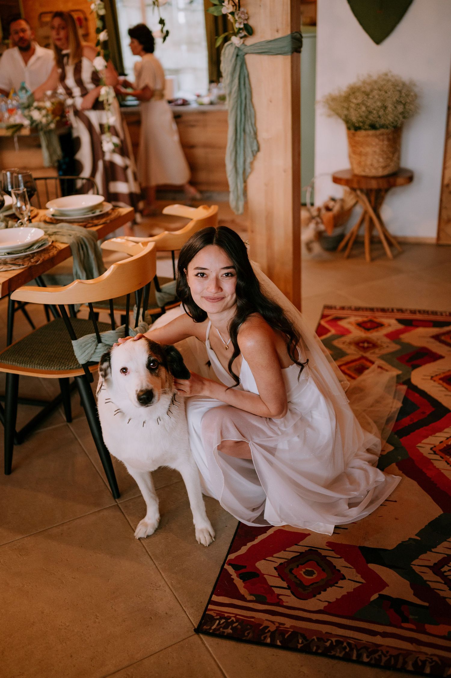 A person in a white dress poses with a white dog on a decorative rug at an indoor event.