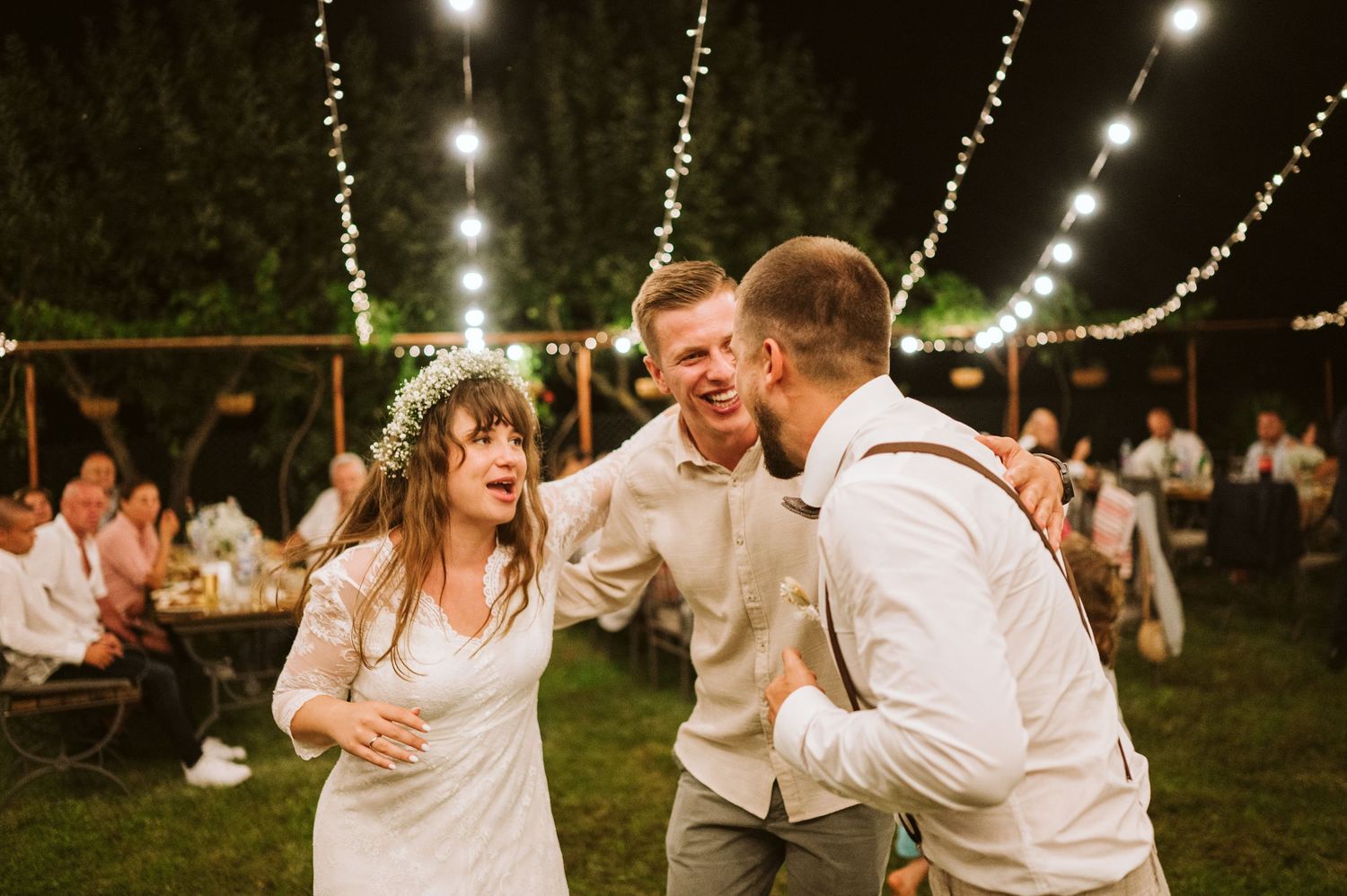 Wedding celebration under string lights with guests dancing and laughing.