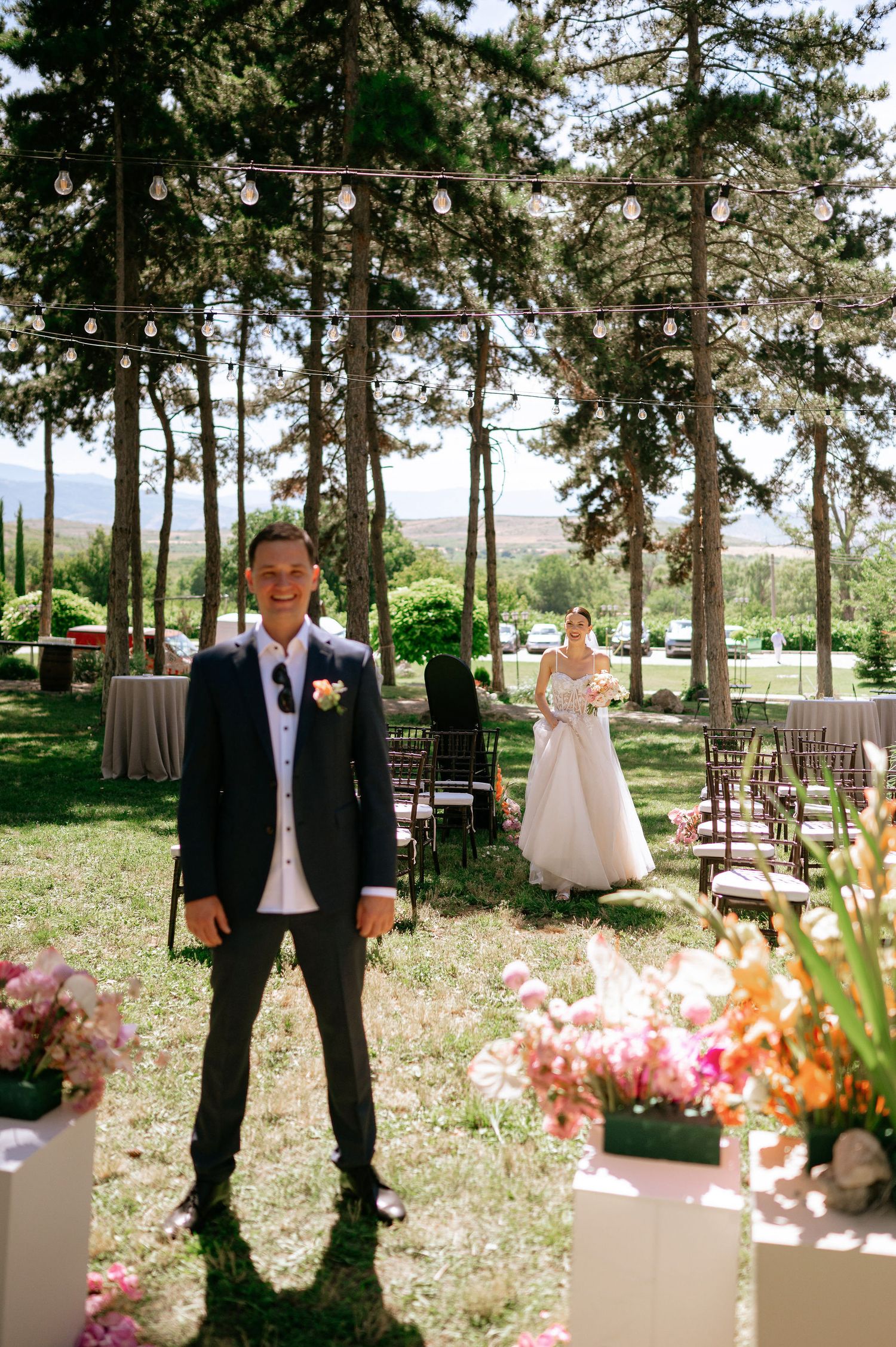 Outdoor wedding venue with string lights and floral arrangements under pine trees.