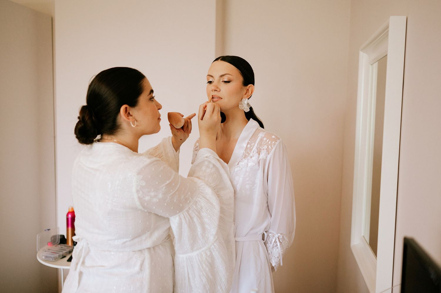 Two people in white robes getting ready for a special occasion in a bright room.