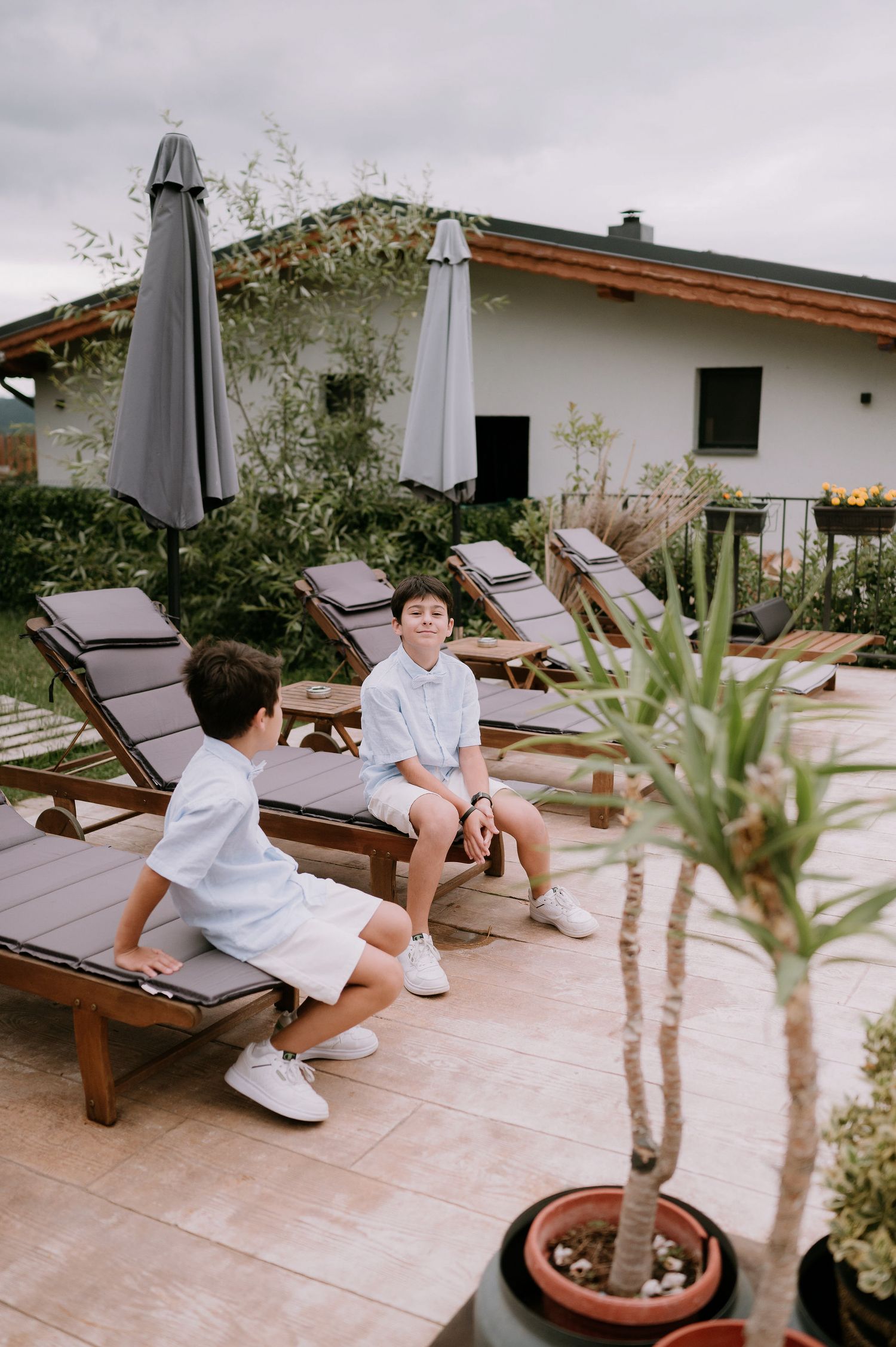 A child in white clothing relaxes on wooden lounge chairs by a pool.