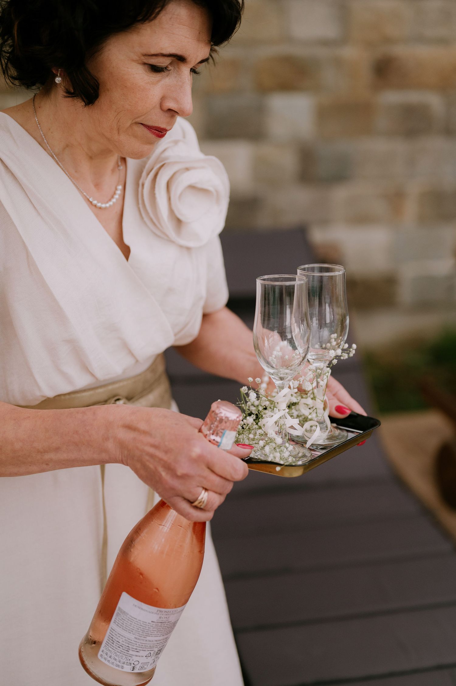 Person in white dress pouring champagne into crystal glasses at outdoor event.