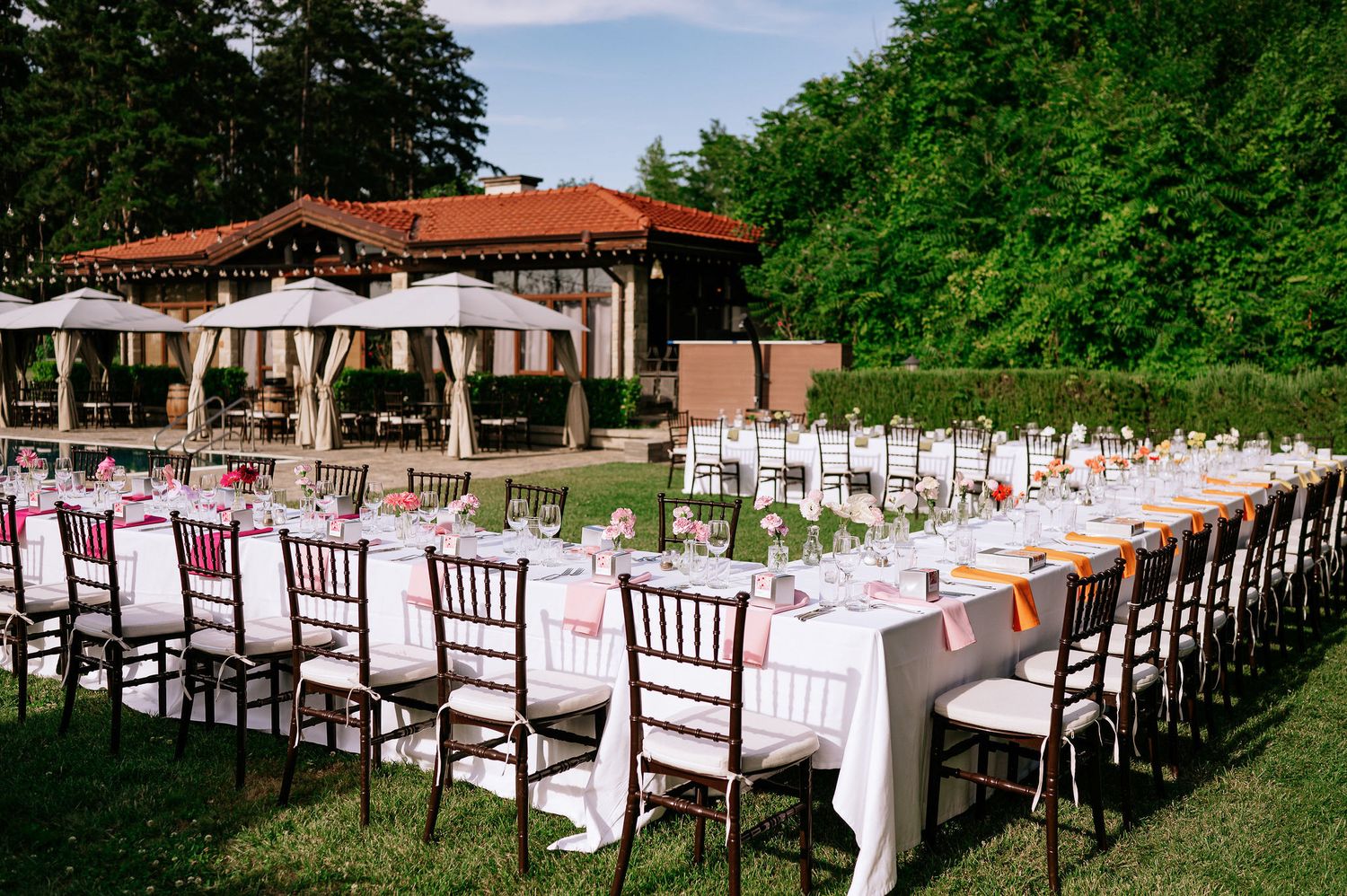 Long banquet tables with white tablecloths and mahogany chiavari chairs set up for outdoor wedding reception.