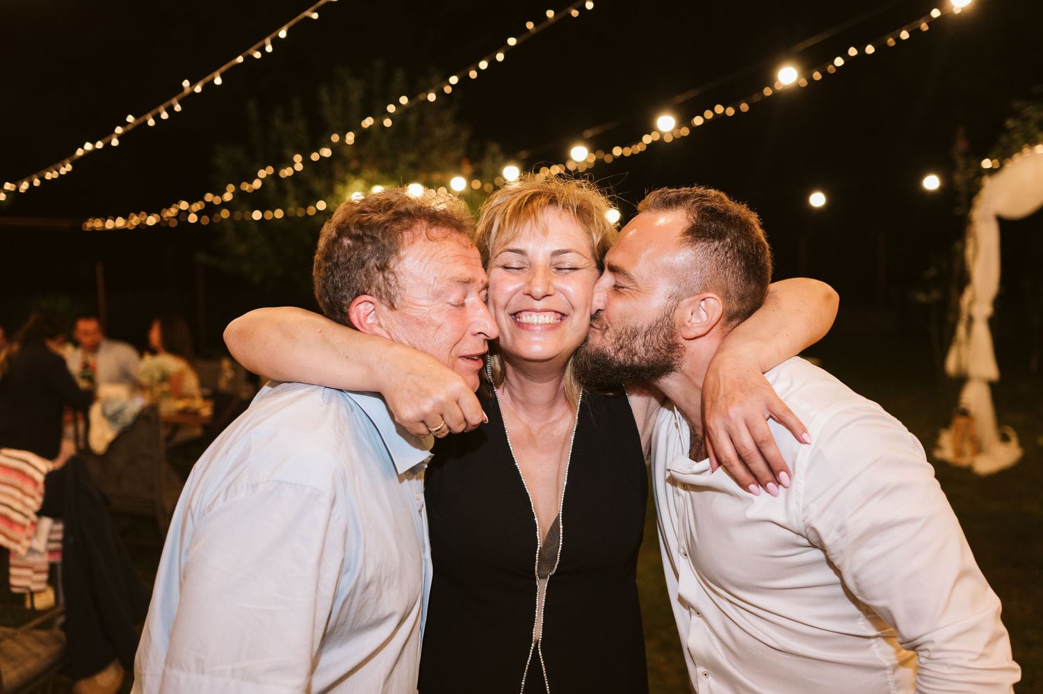 Three people sharing a joyful group hug at a nighttime celebration.