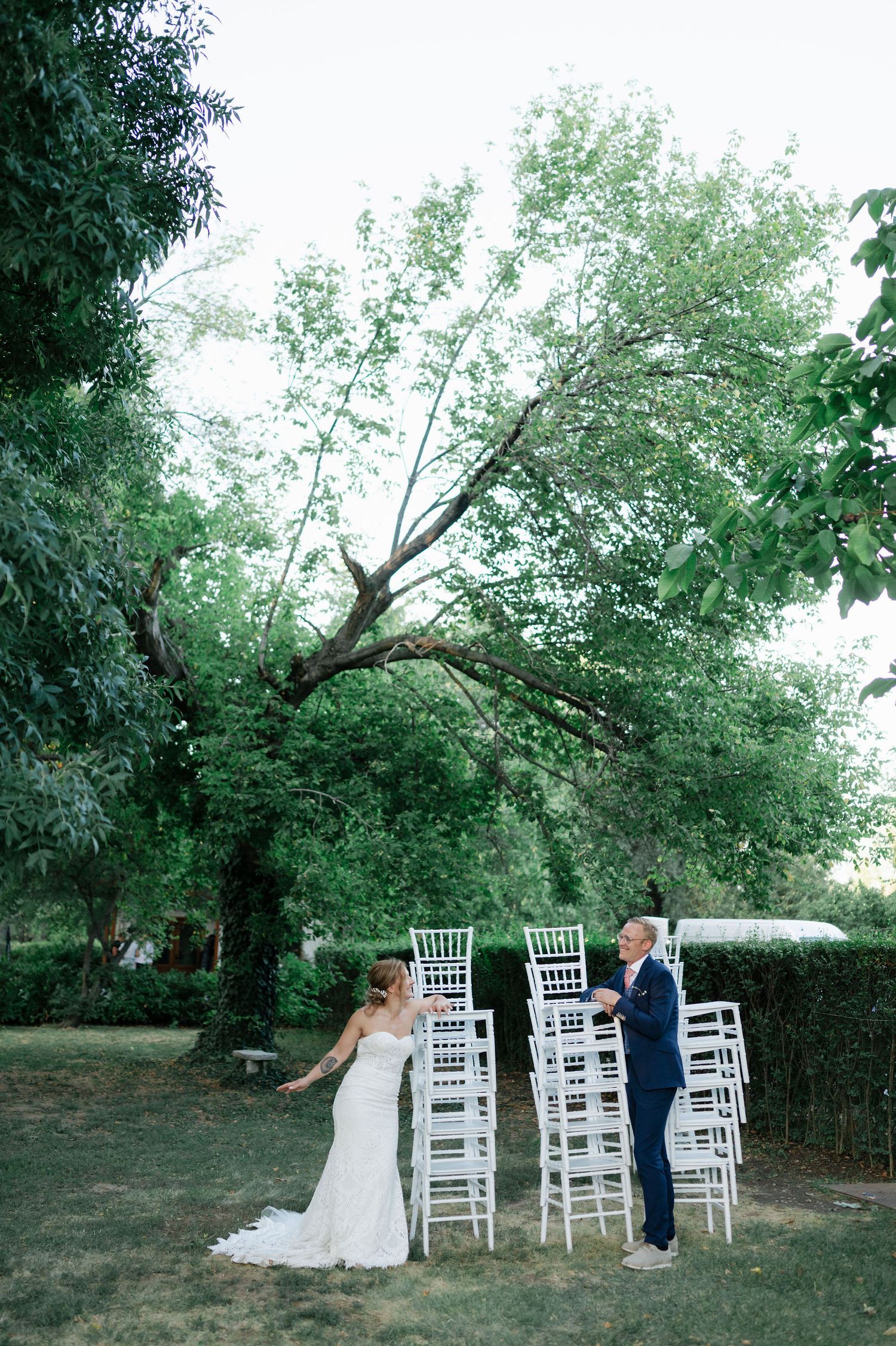 A couple shares a romantic moment among white chairs at an outdoor wedding venue.