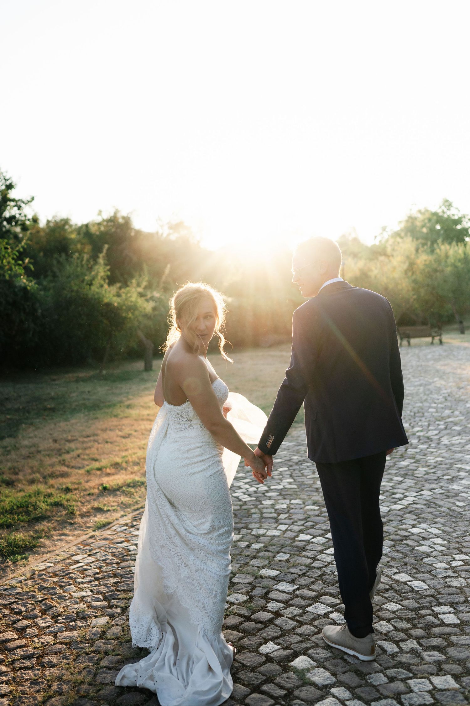 Wedding couple strolling along a garden path with beautiful sunset backlighting.