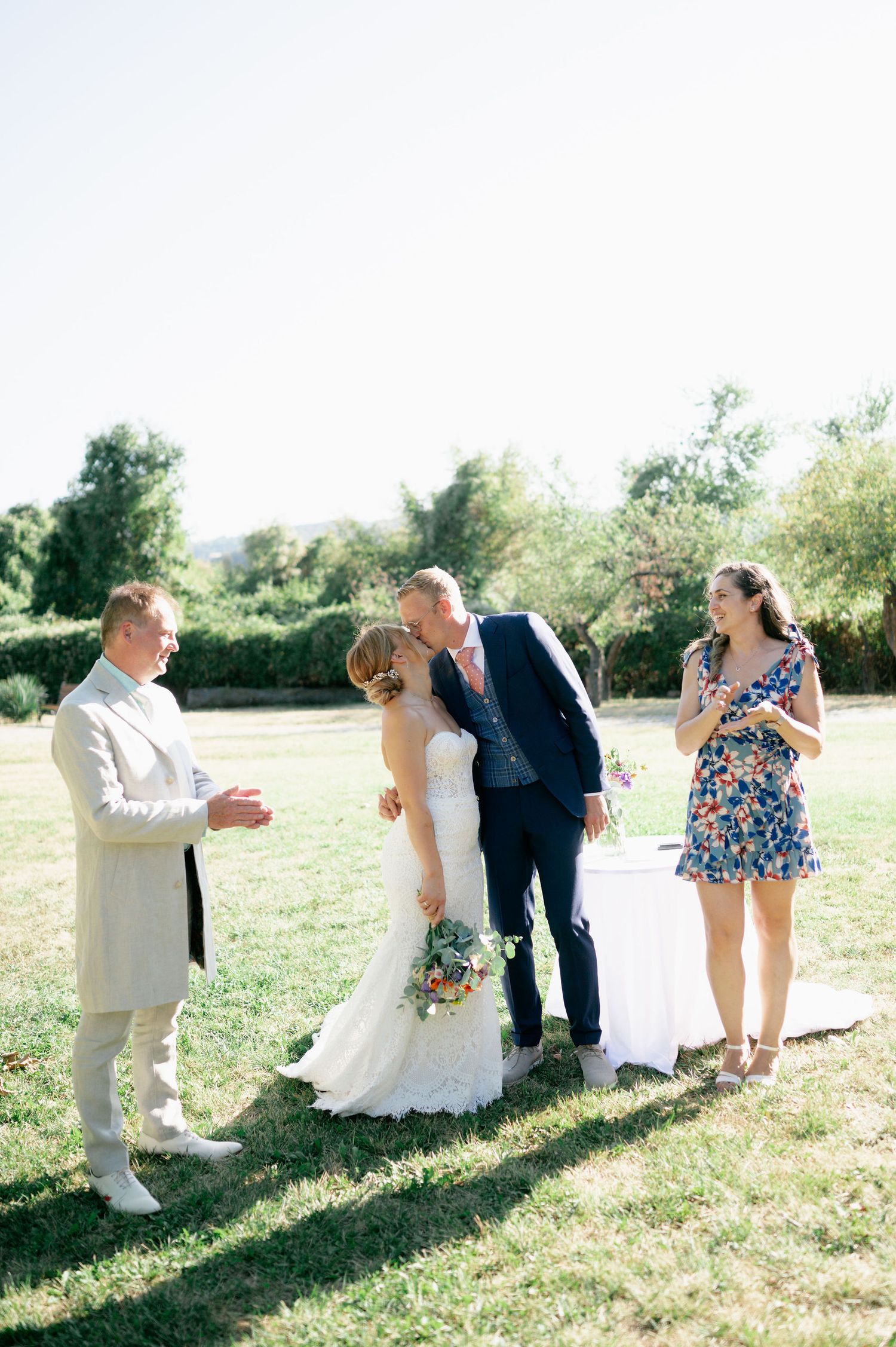 Wedding party members pose and interact on a grassy hillside during an outdoor celebration.