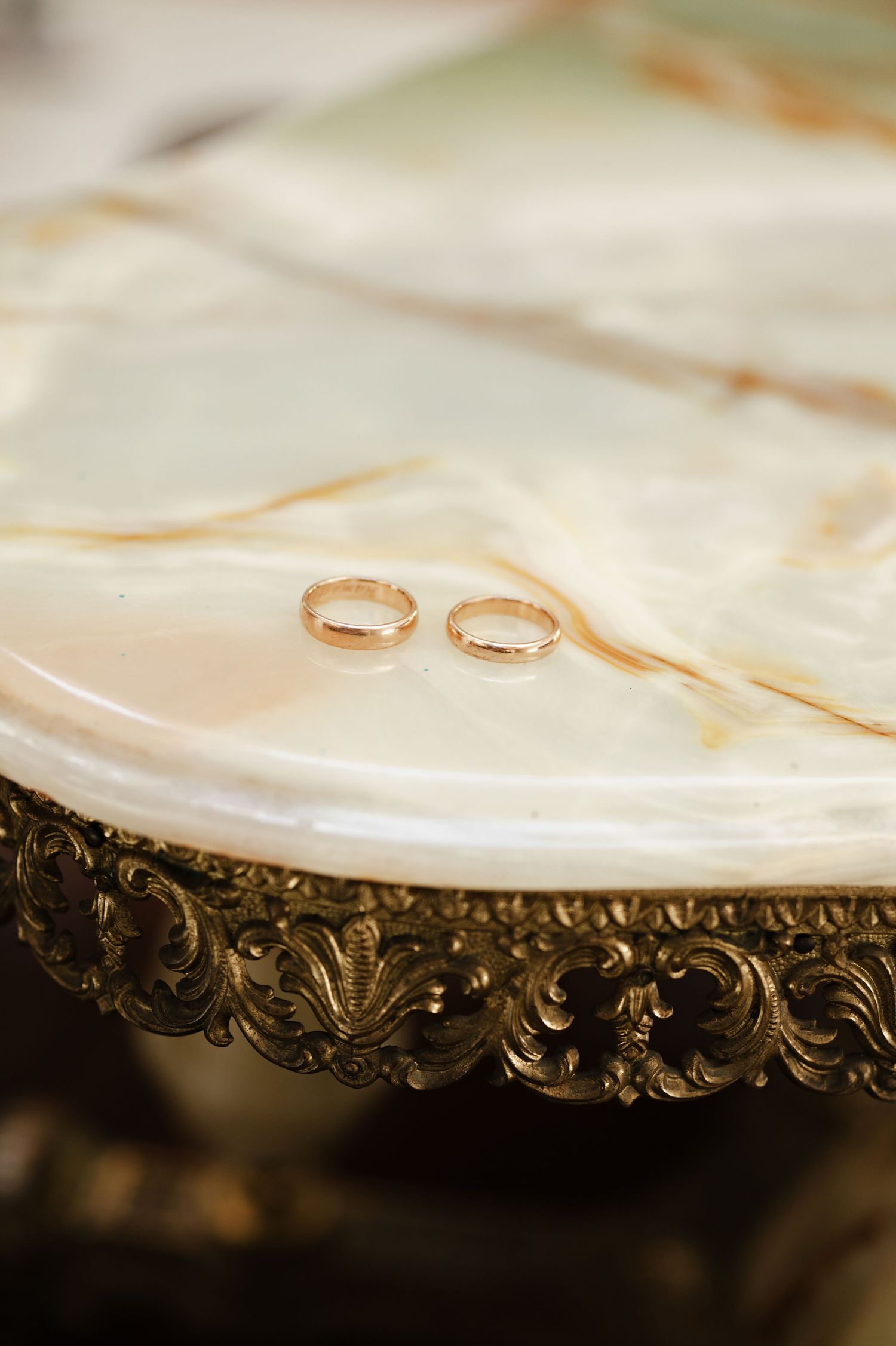 Gold wedding bands displayed on decorative antique plate with intricate metalwork border.