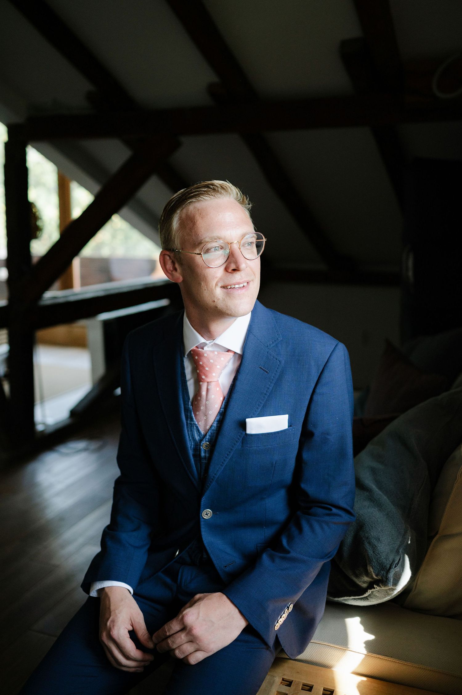 A person in a navy blue suit and tie sits thoughtfully in a room with dramatic lighting.