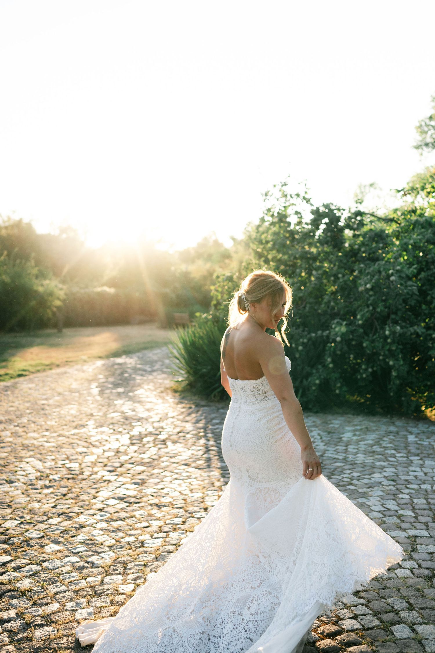 Romantic bridal portrait with flowing dress captured during golden hour on cobblestone ground.