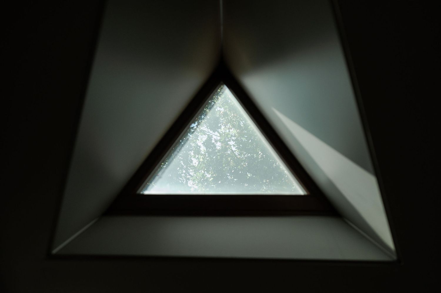 A triangular skylight window with a dark frame against a bright background.