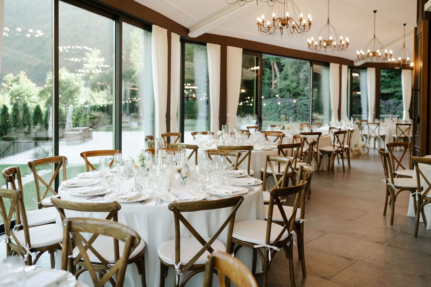 Elegant wedding reception hall with crystal chandeliers and cross-back chairs.