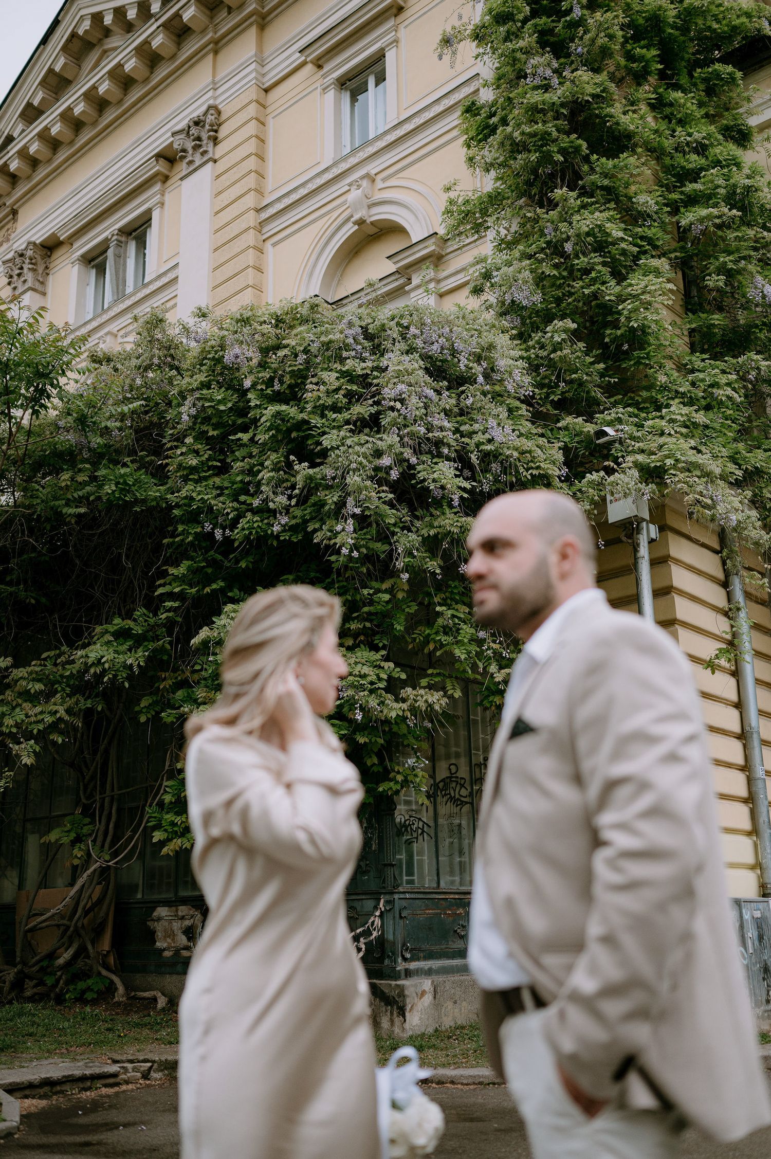 Couple in matching light outfits posing playfully outside historic building.