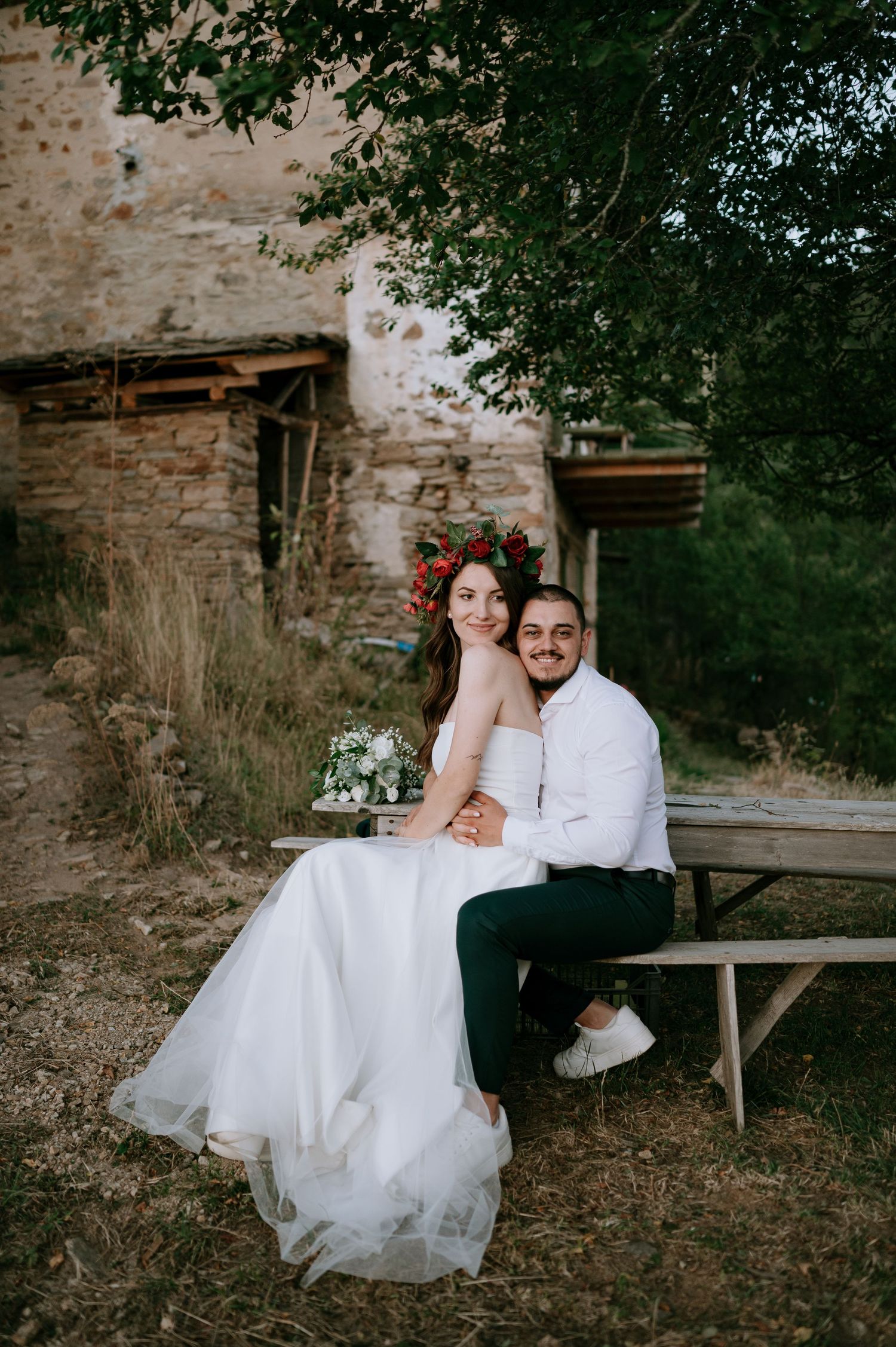 Romantic wedding portrait by rustic stone wall with wooden bench.