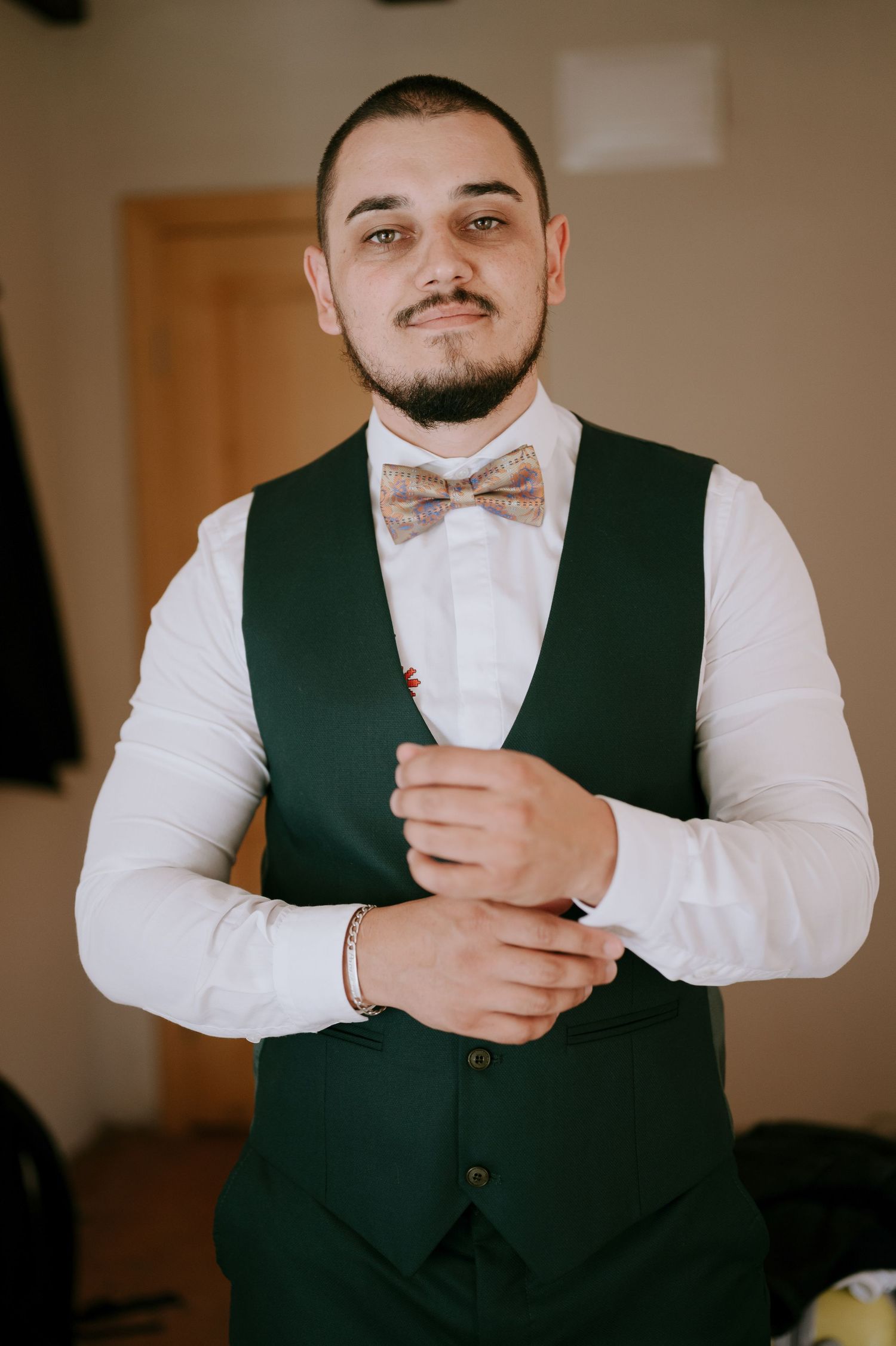 A close-up shot of someone adjusting their white bowtie with a dark green vest.