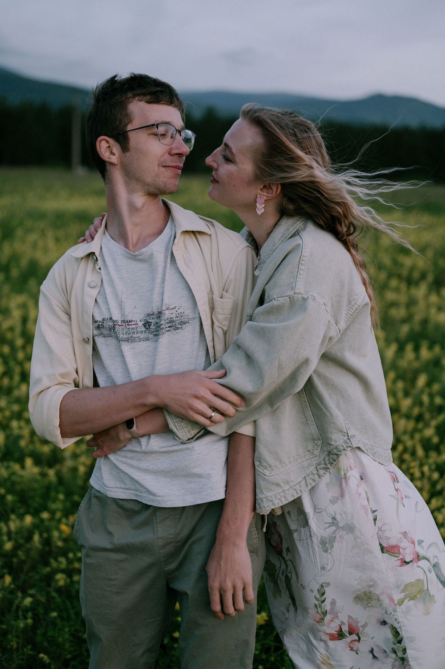 A romantic couple embraces in a blooming yellow flower field on an overcast day.