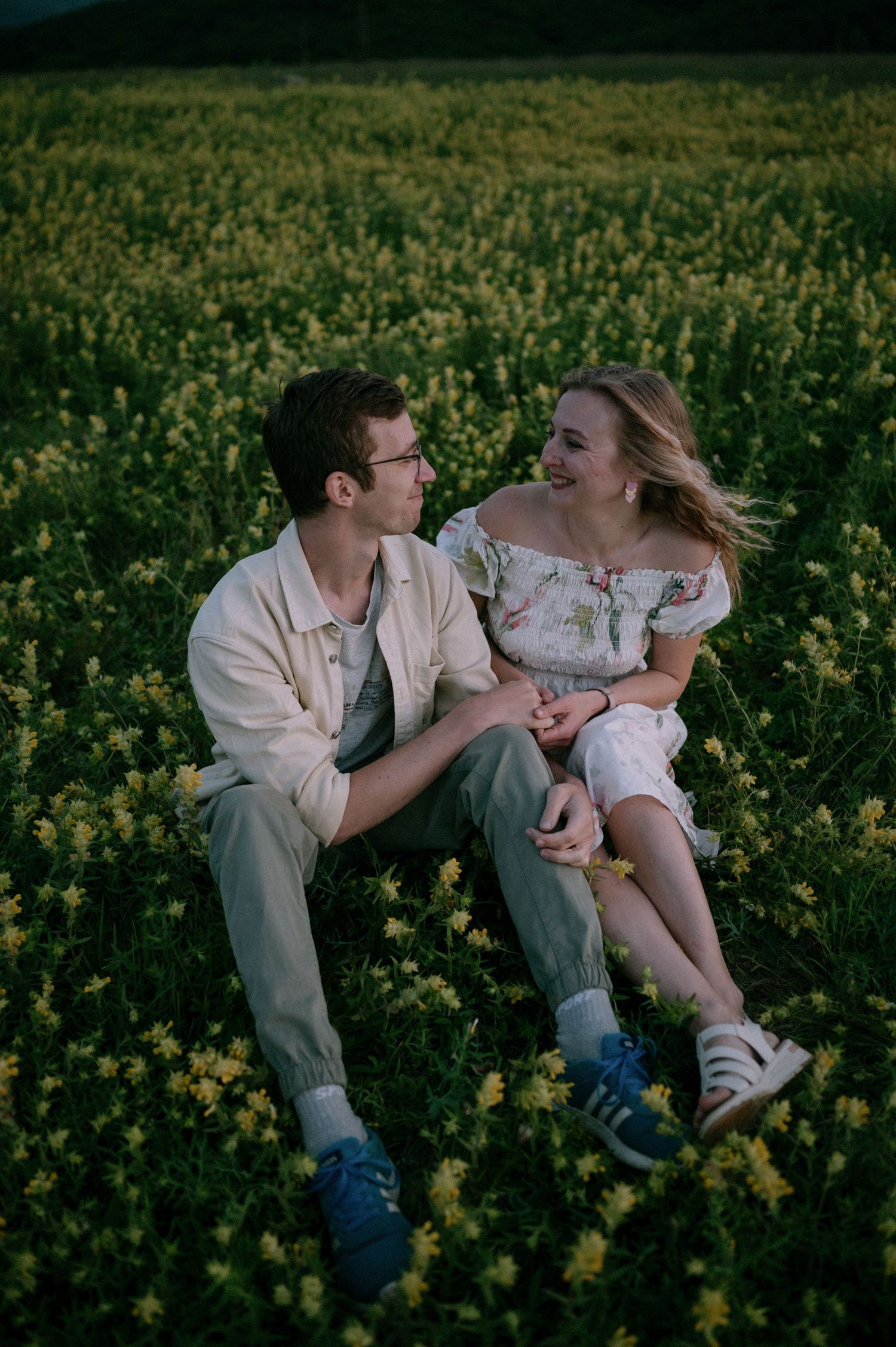 Playful couple laughing together while lying in a field of bright yellow flowers.