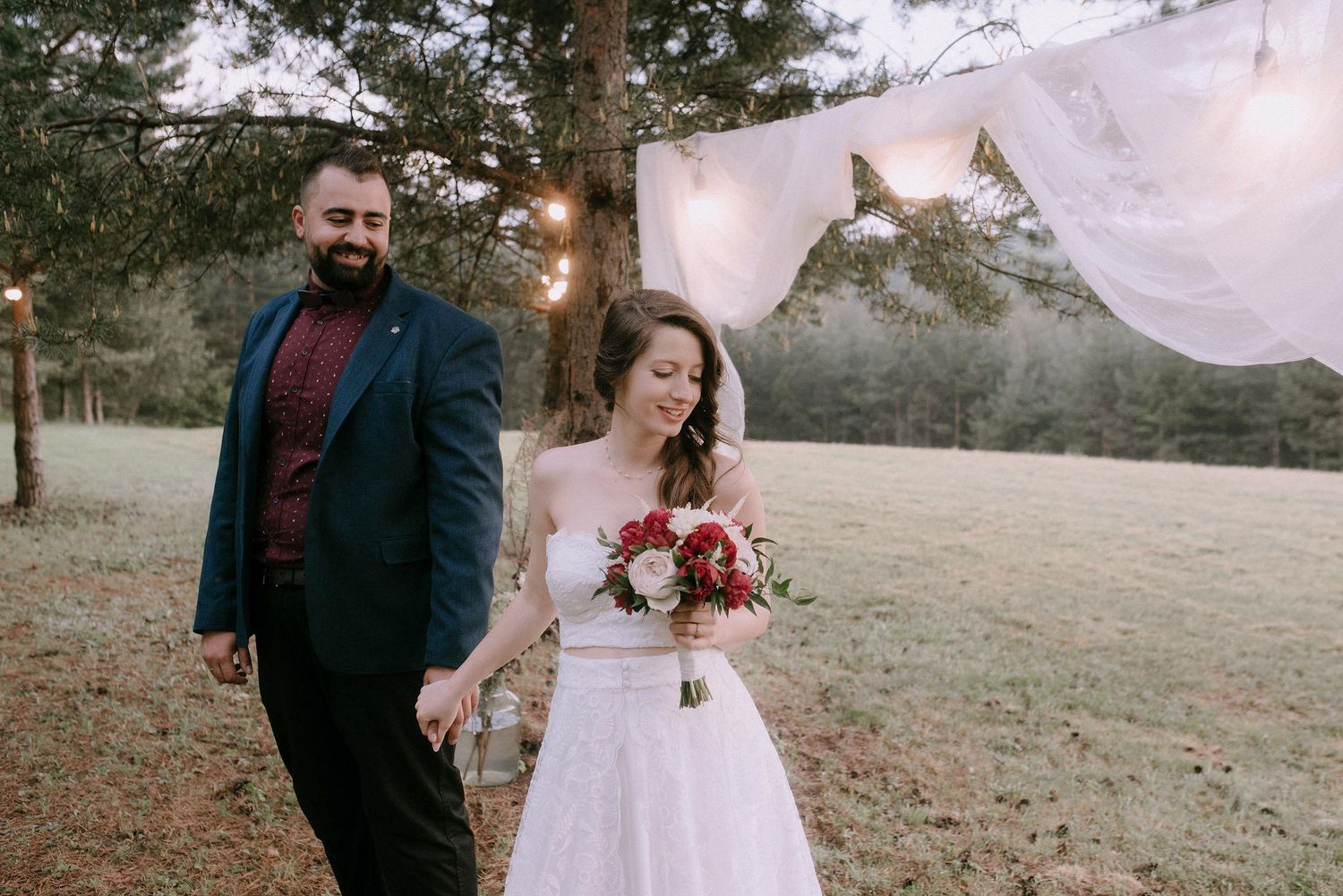 Elegant outdoor wedding ceremony with white fabric backdrop and floral arrangements.
