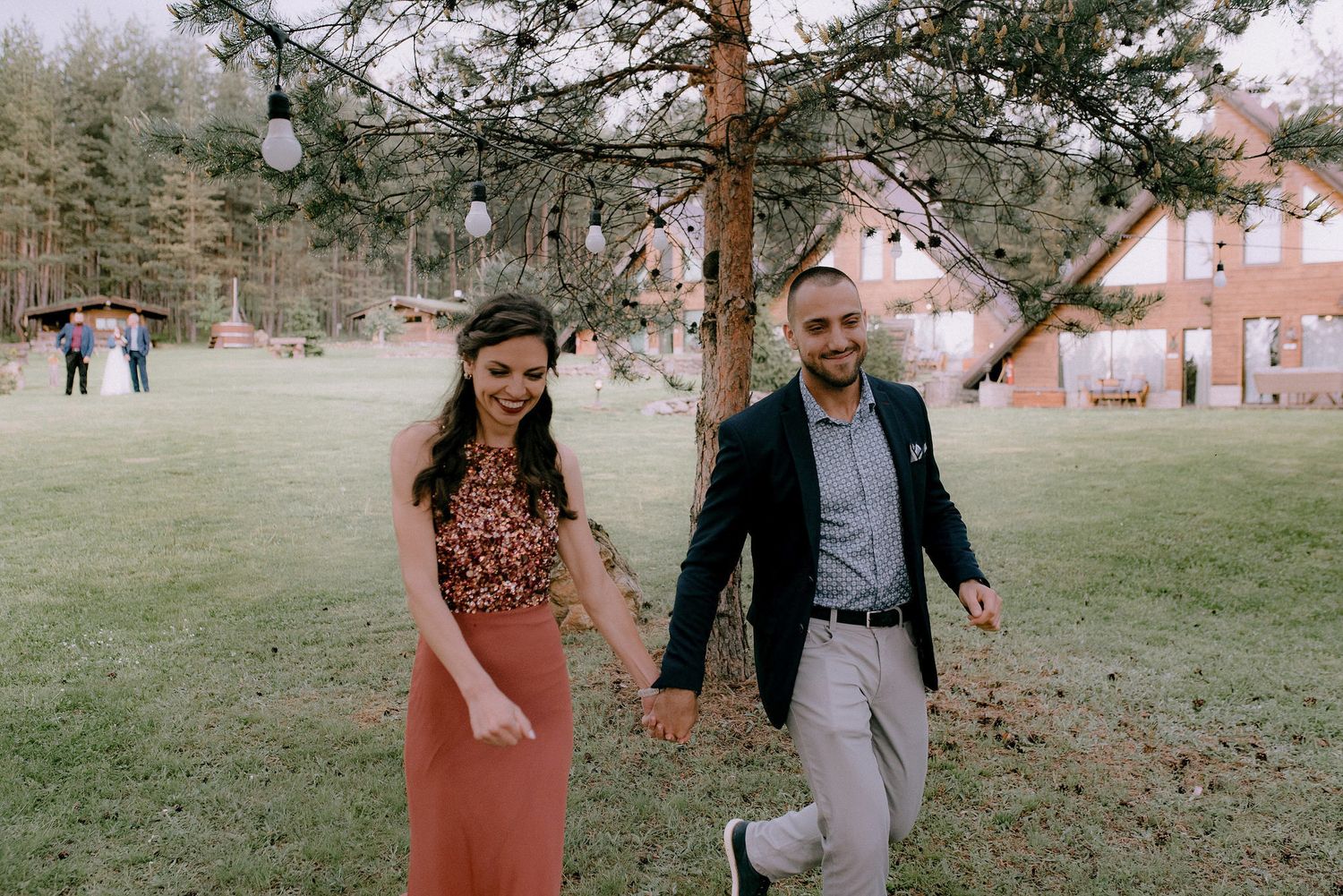 Wedding celebration taking place on a green lawn surrounded by tall pine trees.