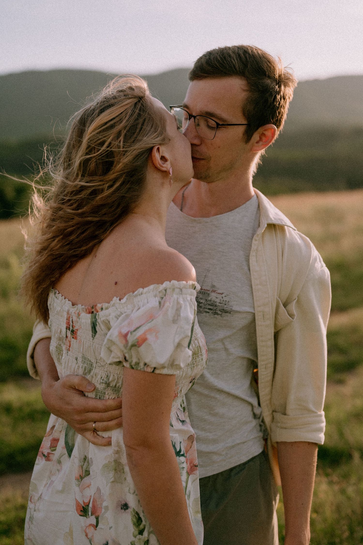 Romantic couple sharing kisses and embraces in a mountain field during sunset.