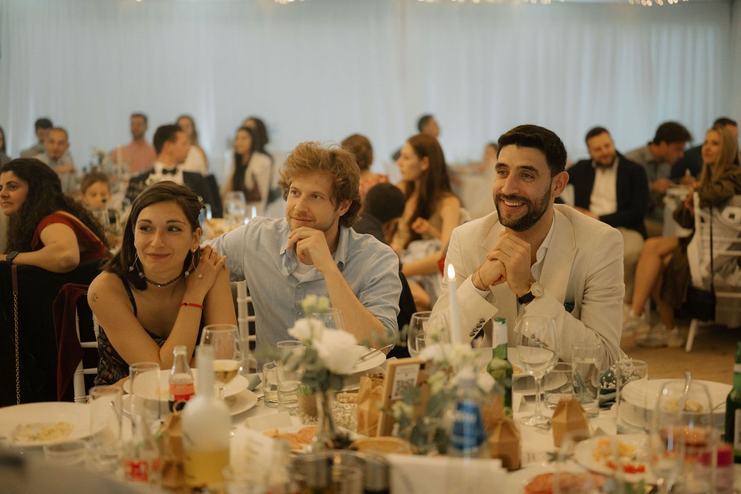 Guests smiling and laughing at a wedding reception dinner, seated at a decorated table in an elegant venue.