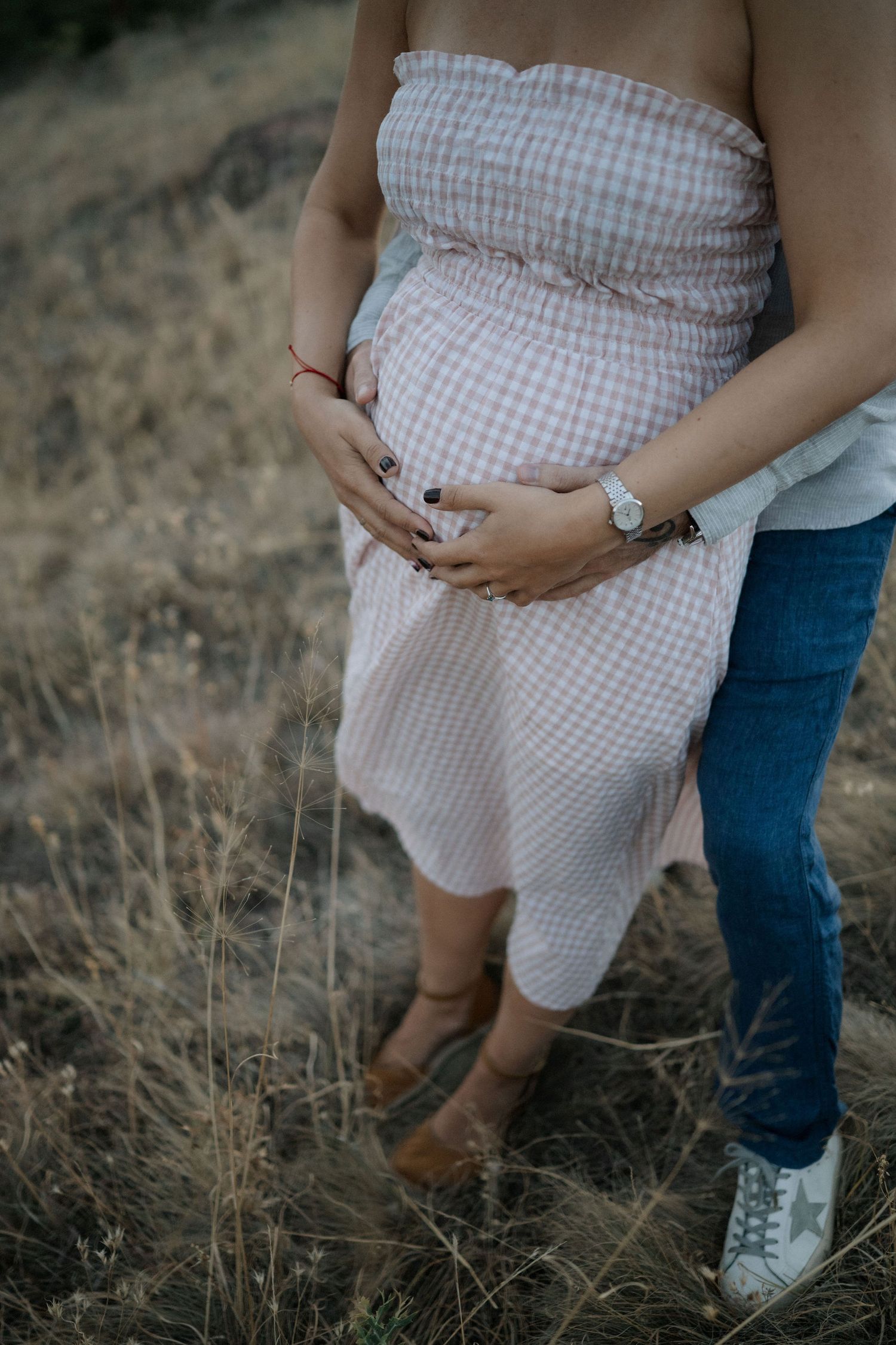 Close-up view of a couple in a field wearing casual clothing, with a gingham dress and jeans visible.