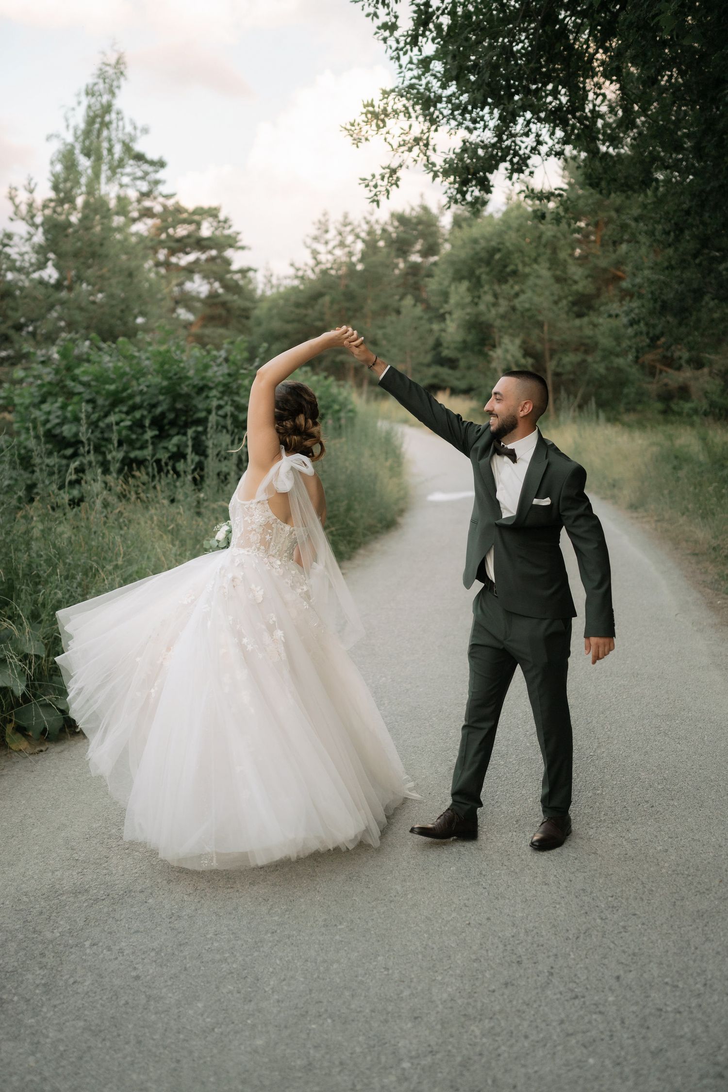 A couple performs an elegant dance spin in their wedding attire on a rustic outdoor path.