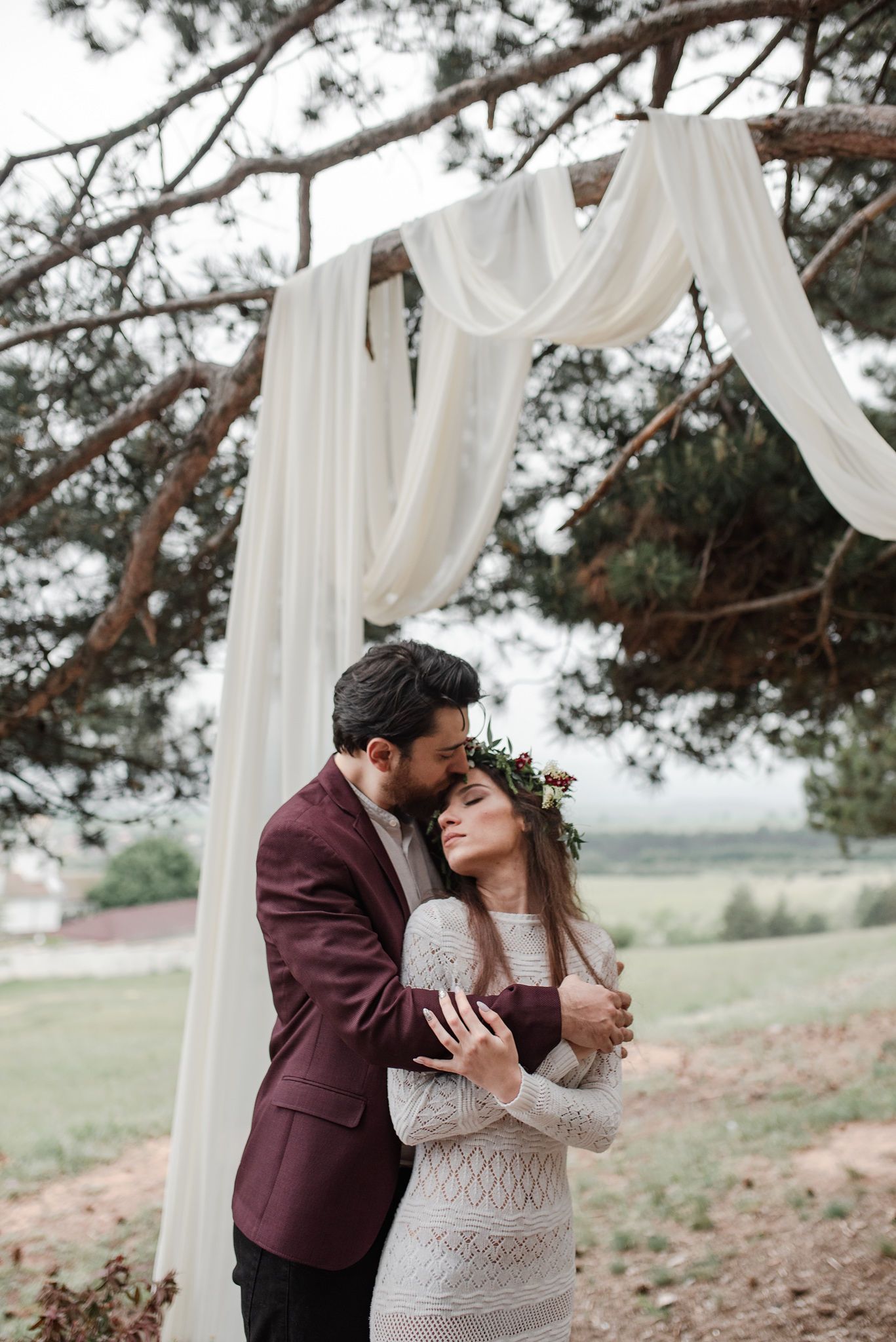 A romantic outdoor wedding scene with white drapes and pine trees in the background.