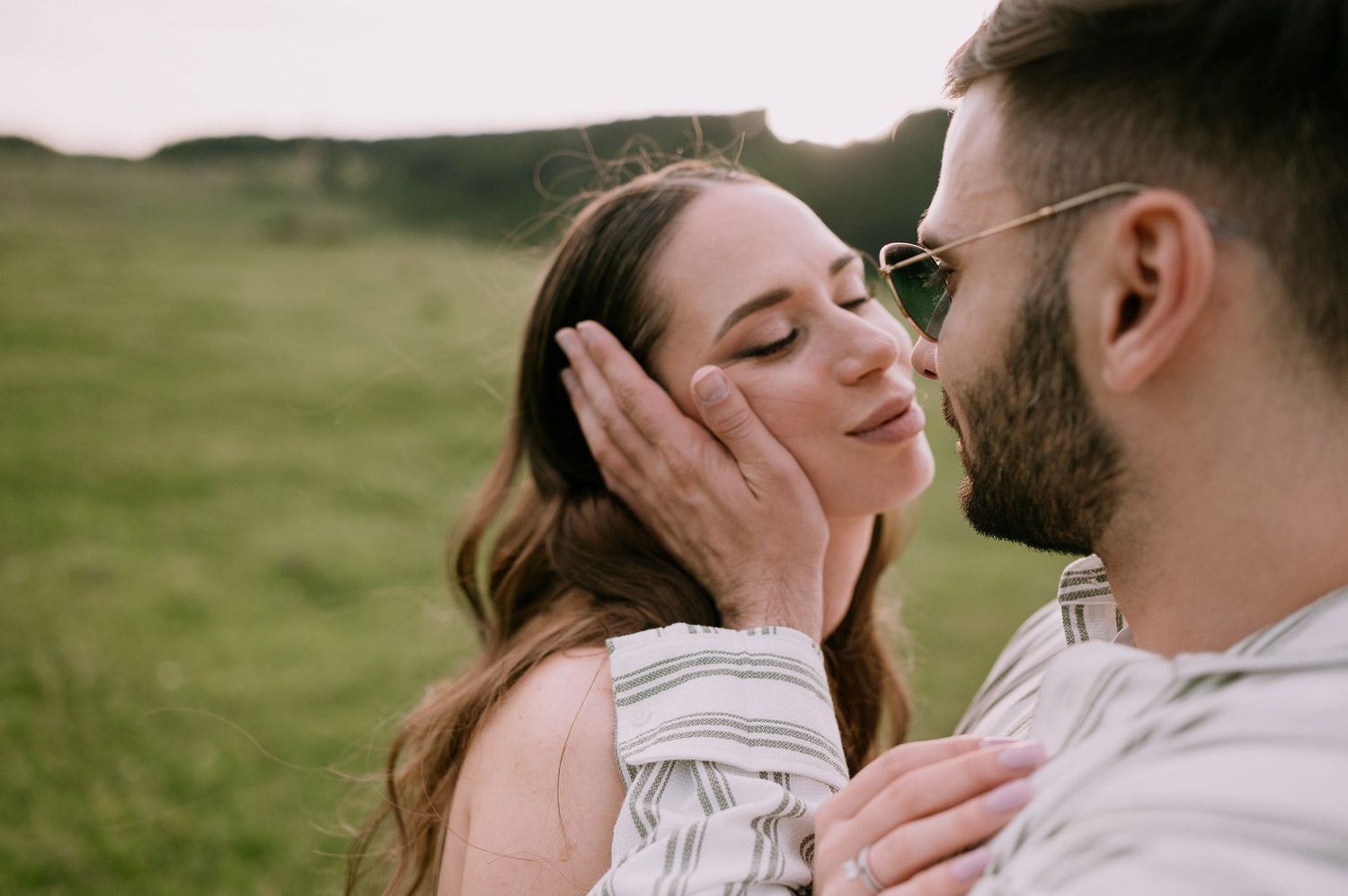 A romantic couple shares tender moments in a series of intimate outdoor portraits in a grassy field.