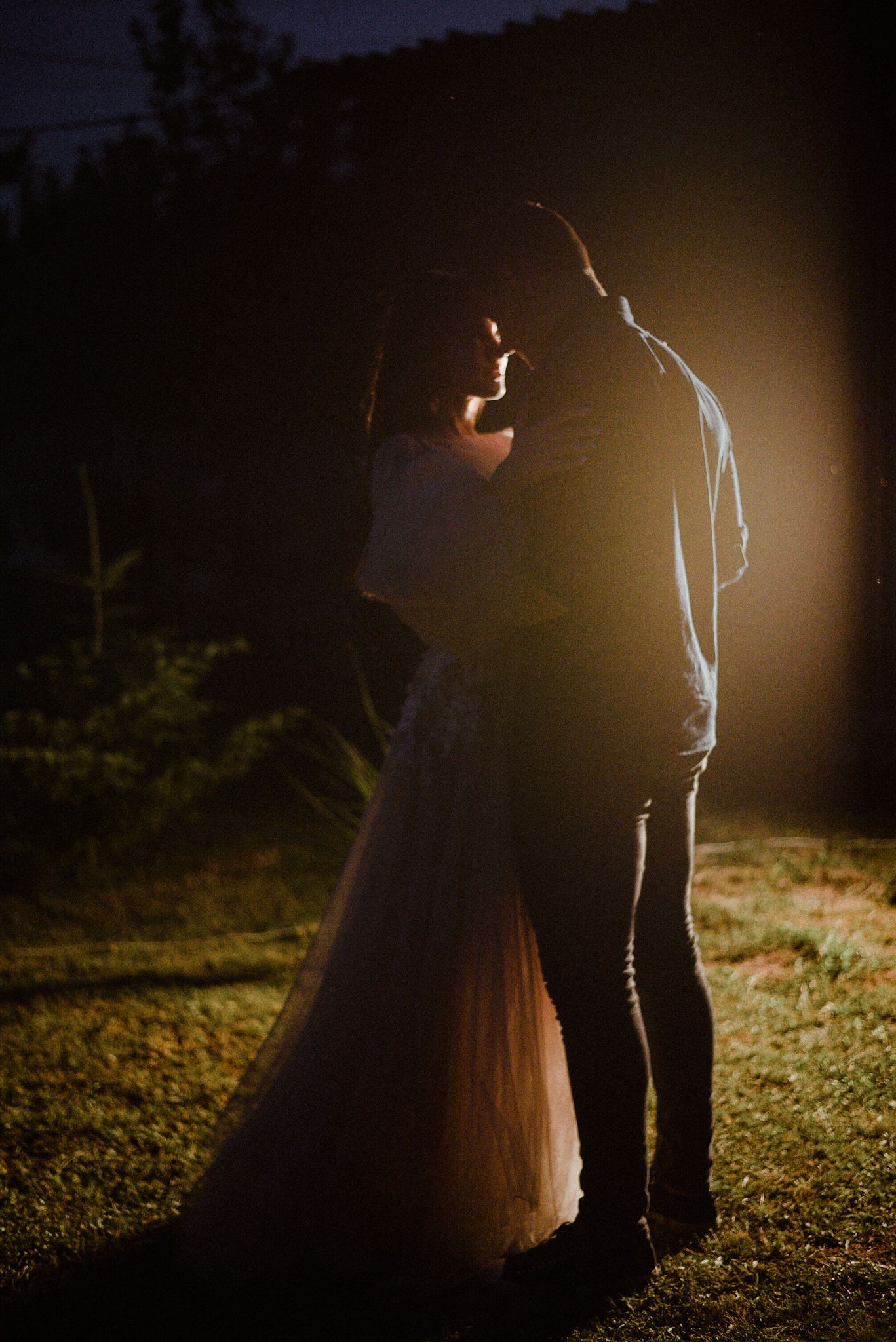 Silhouetted couple standing close together in dramatic nighttime lighting creating a romantic outdoor atmosphere.