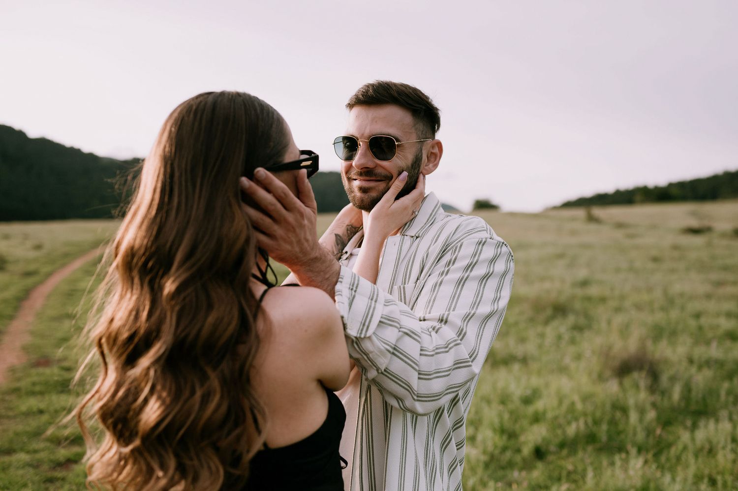 A couple embraces in a sunny meadow while wearing coordinated white and striped outfits.