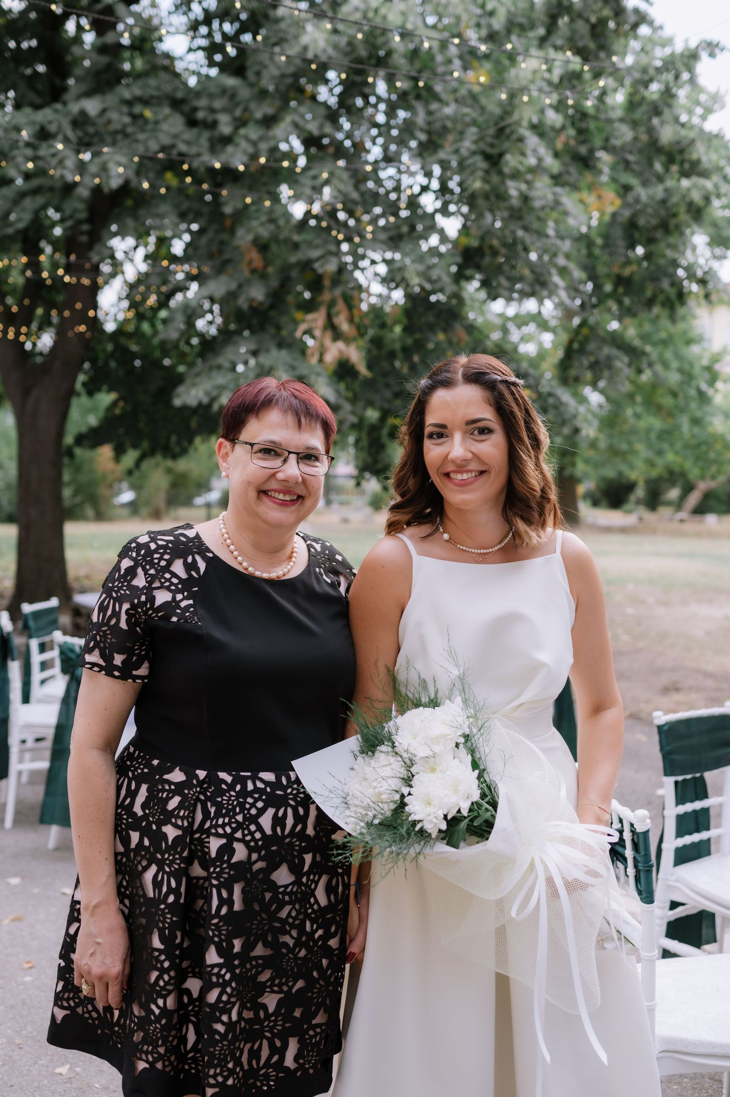 Two people share a joyful moment together outdoors at a wedding celebration with trees in the background.