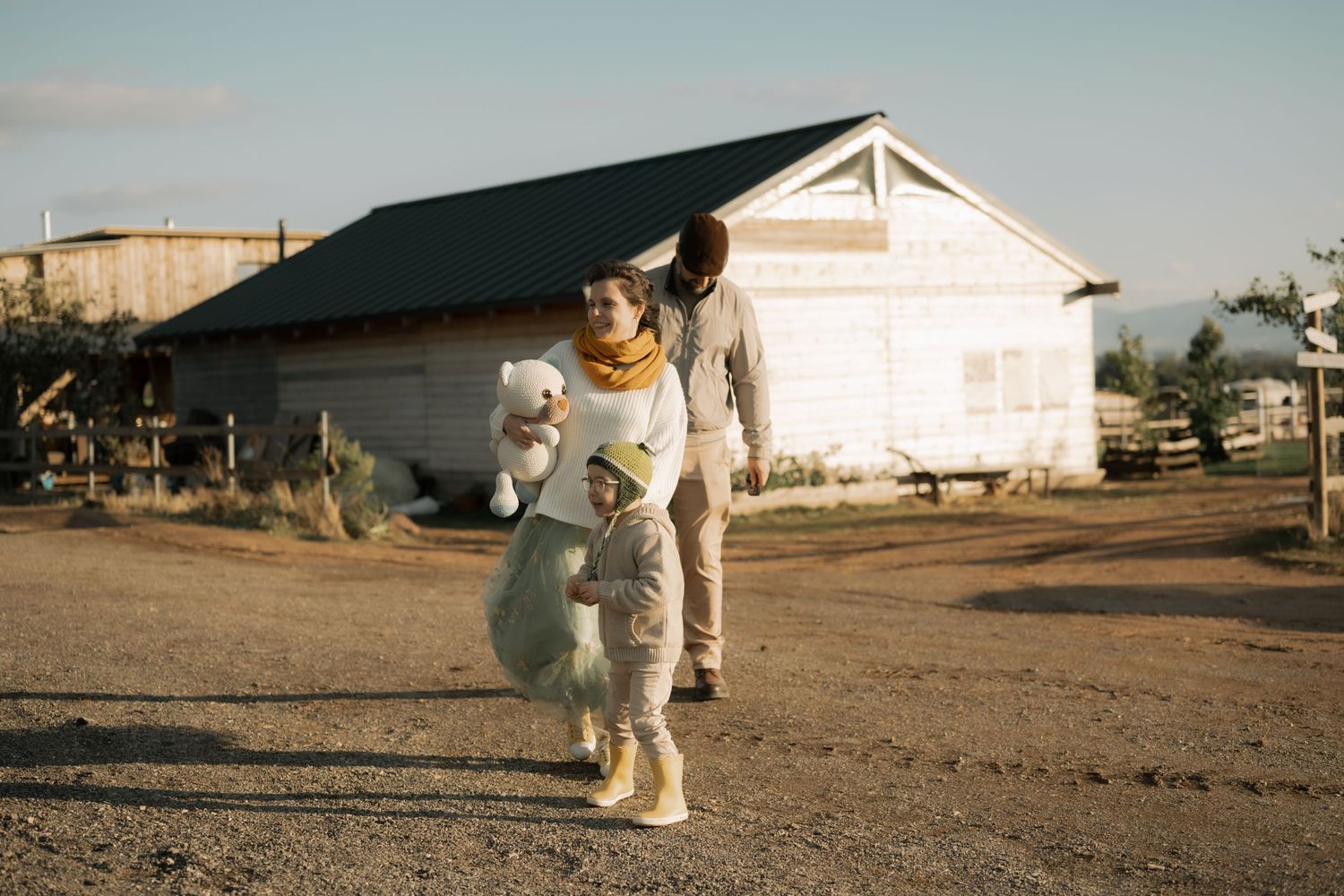 Two people in astronaut suits walk on a dirt path near a white building during golden hour.